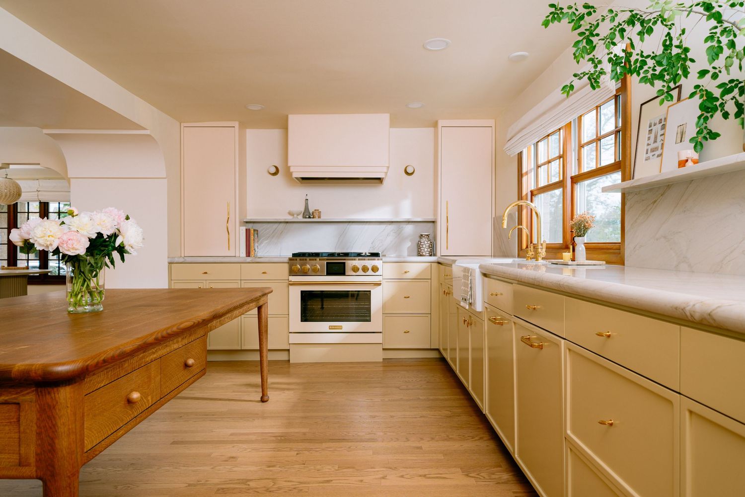 Bright kitchen with cream cabinets, gold hardware, white range, marble counters, wood island, and natural light from windows.