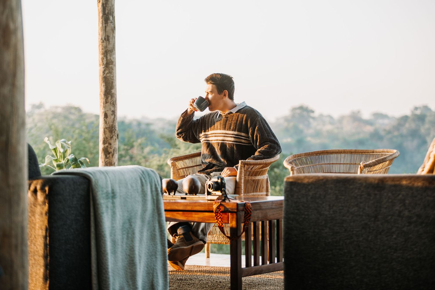 Someone enjoying a hot drink while relaxing on a balcony with wicker furniture and scenic views at sunset.