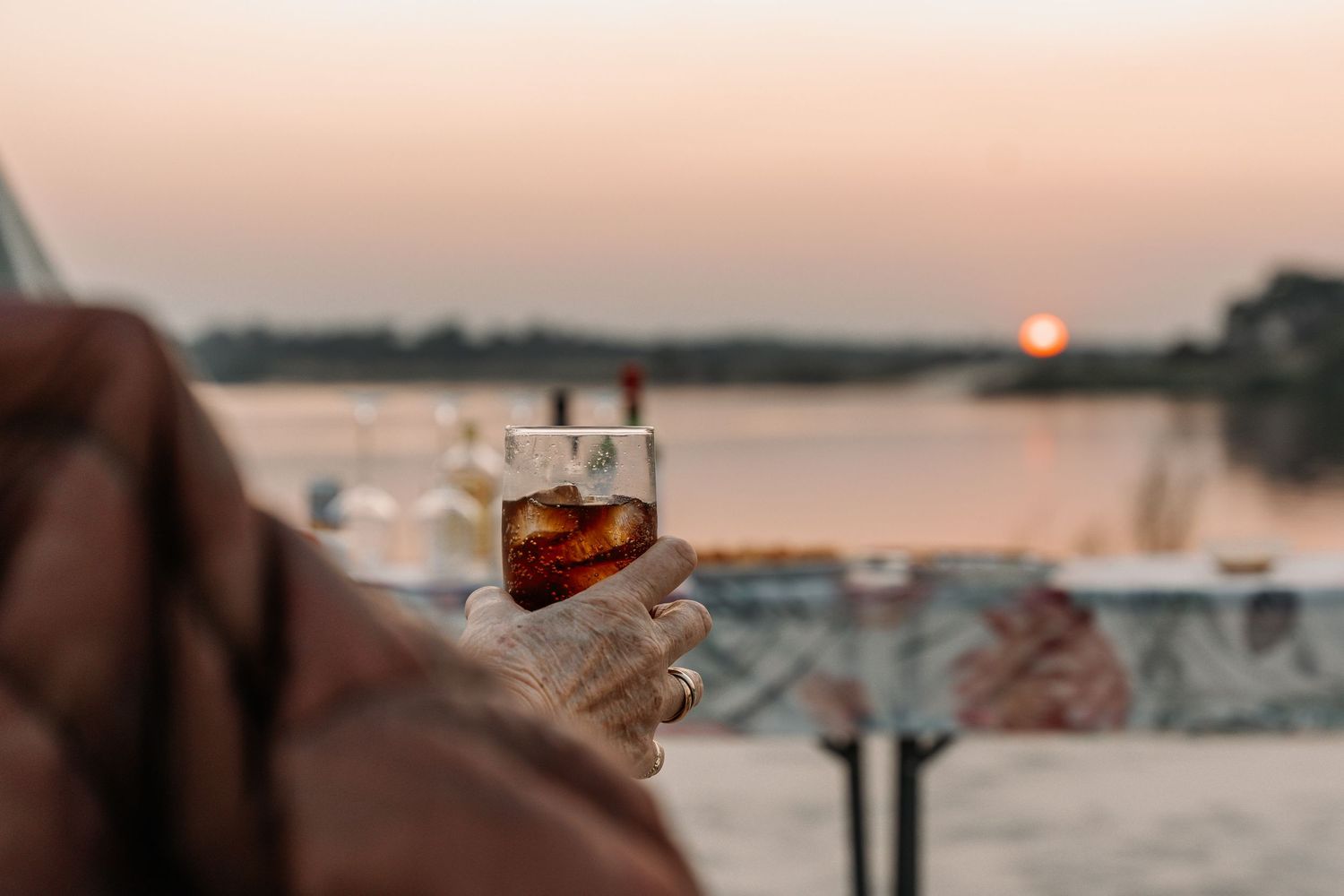 A glass of wine held against a sunset waterfront view, creating a romantic evening ambiance.