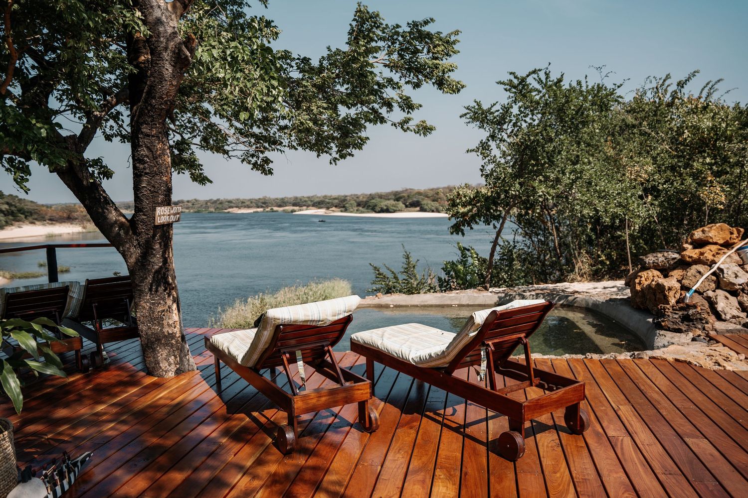 Wooden deck overlooking a scenic coastal view with trees providing shade on a sunny day.