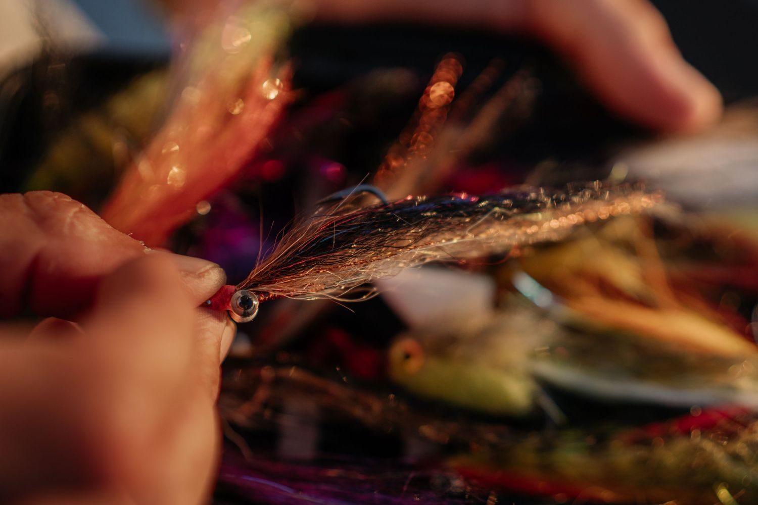 Close-up of hands tying a colorful fly fishing lure with feathers and thread.