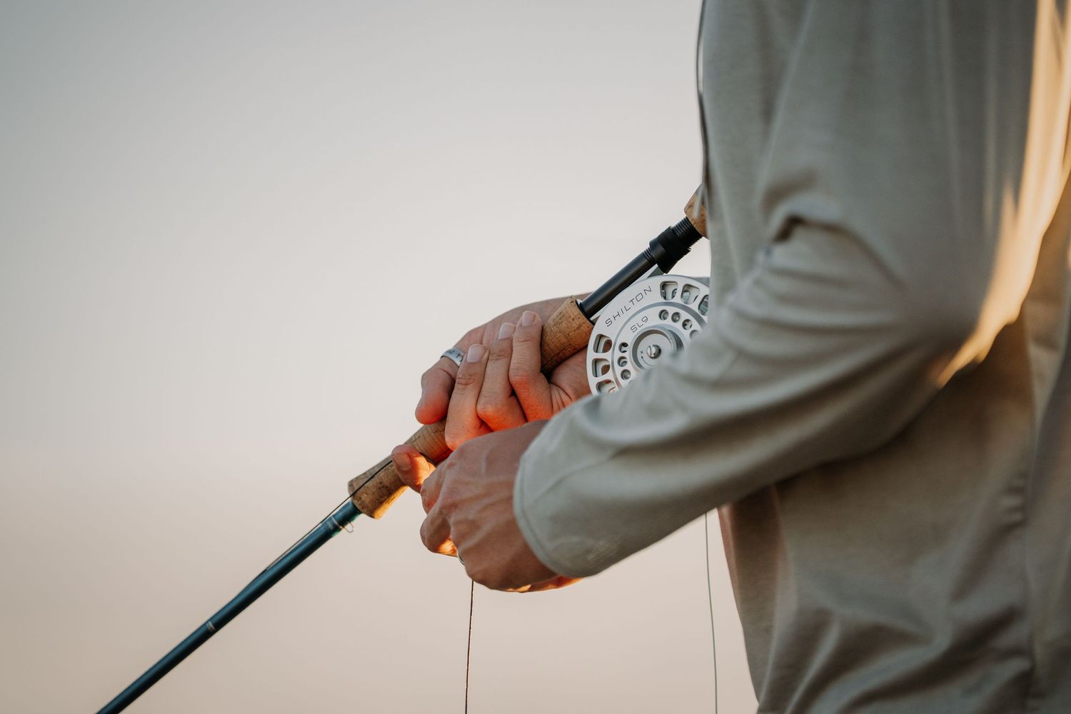 Person holding a fishing rod with fishing line, wearing a gray long-sleeve shirt at dusk.