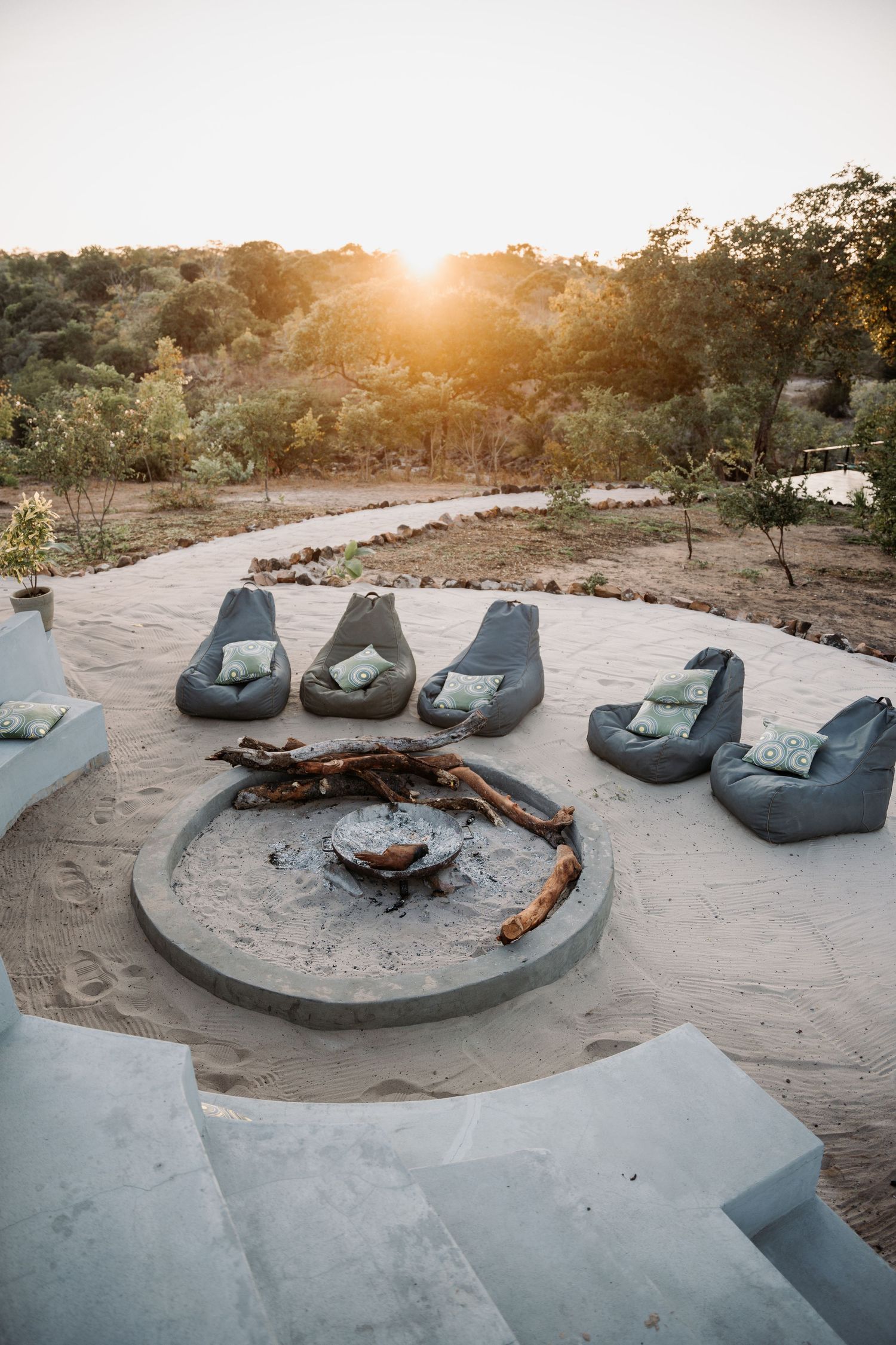Modern curved concrete fire pit with comfortable lounge chairs arranged around it at sunset in a desert setting.