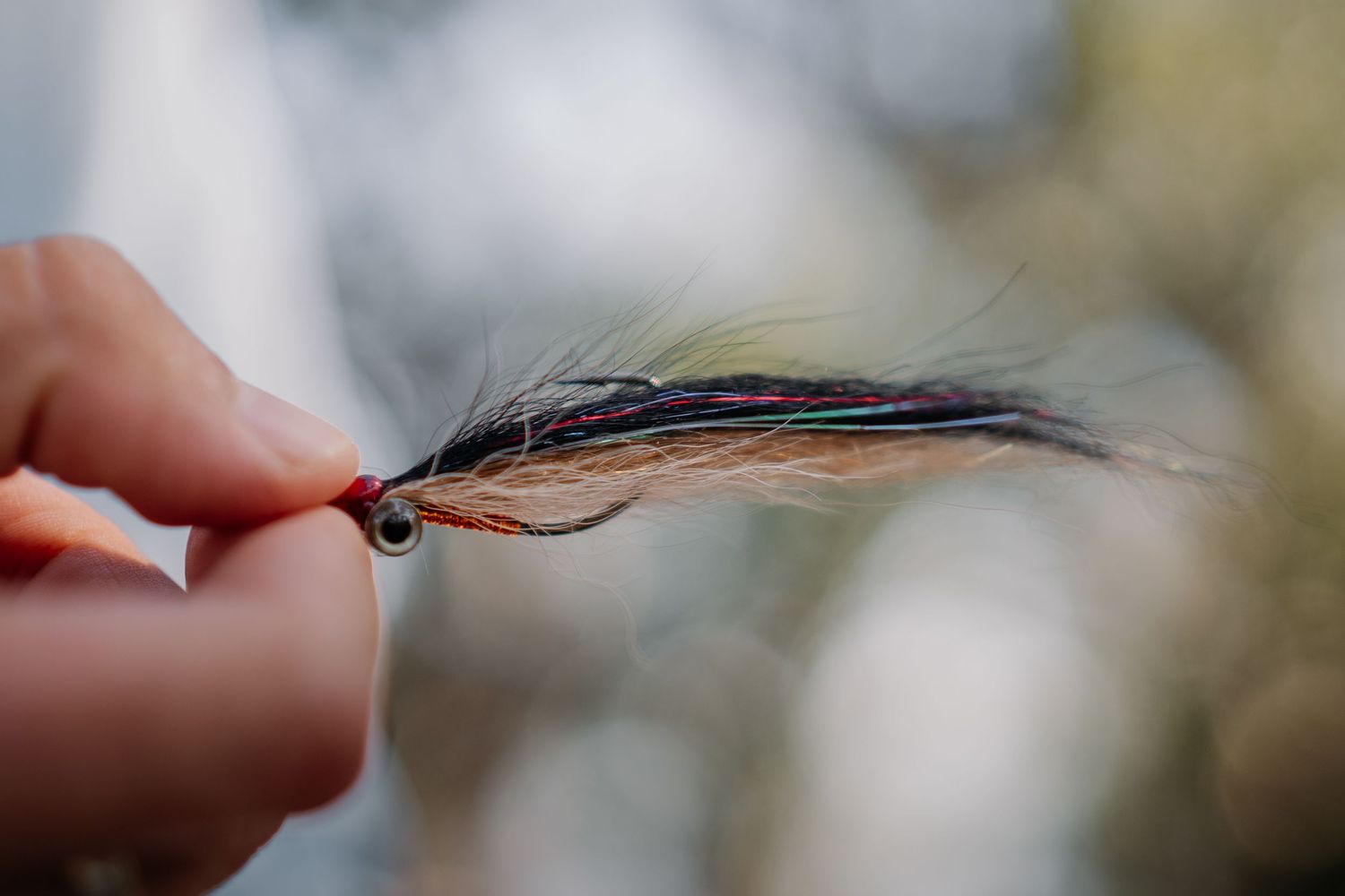 Close-up of a hand holding a handmade fly fishing lure with natural feathers and red thread wrapping.