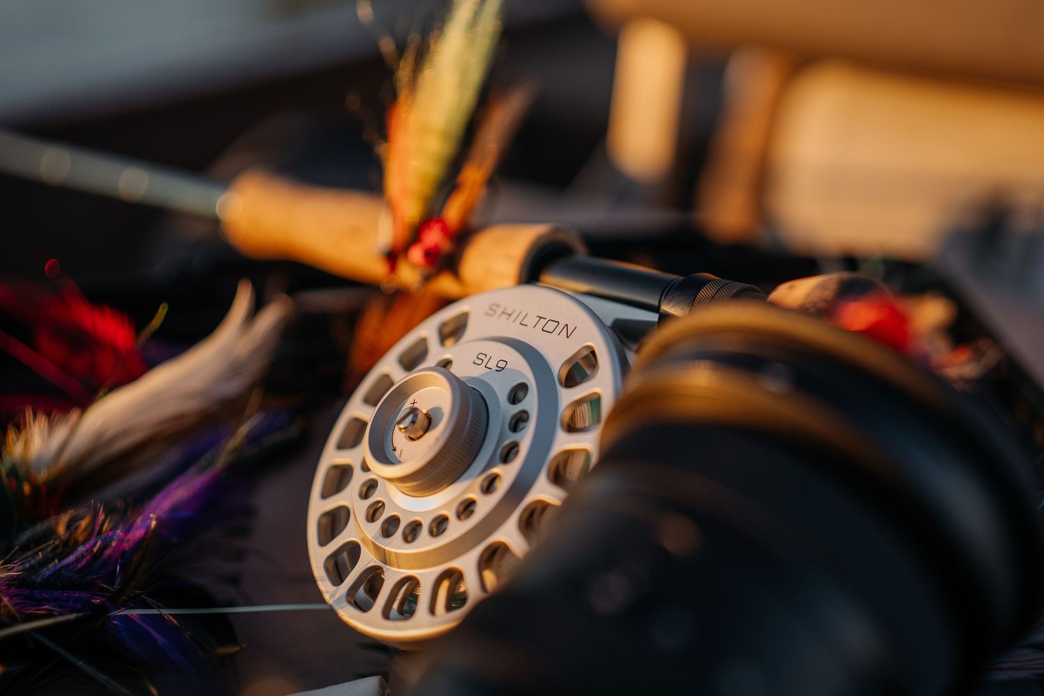Close-up of a Hamilton fly fishing reel with colorful fly lures in warm golden light.