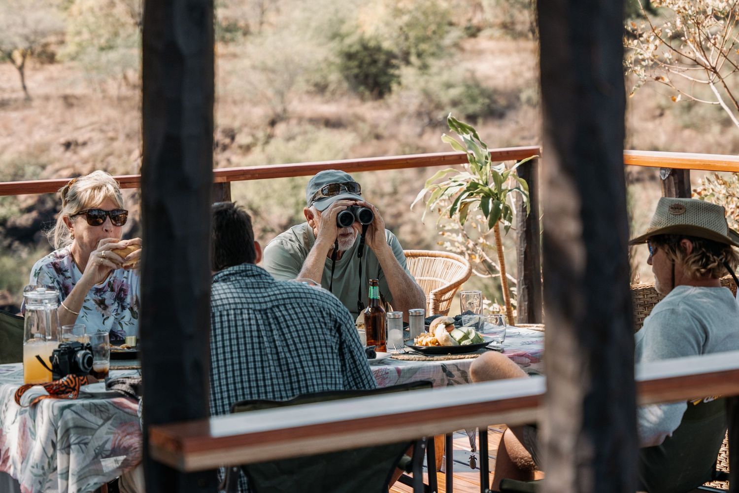 Guests relax at a rustic outdoor bar area with wooden beams during golden hour.