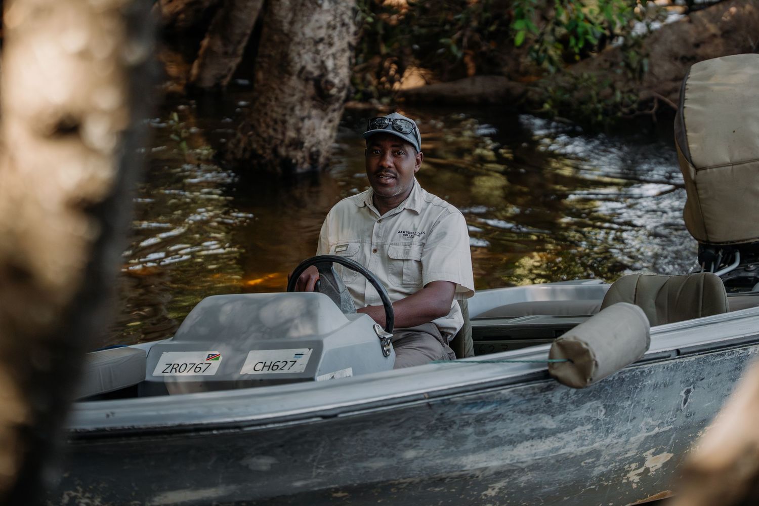 Man sitting in a small aluminum motorboat on a calm river surrounded by trees.
