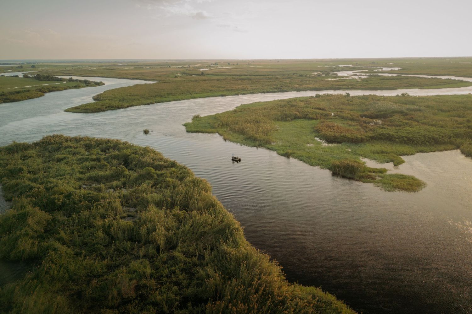 Aerial view of a winding river delta with lush green islands and calm waters at dusk.