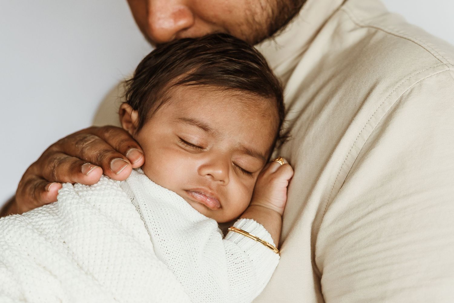 A sleeping newborn baby wrapped in a white blanket resting peacefully on a parent's chest.