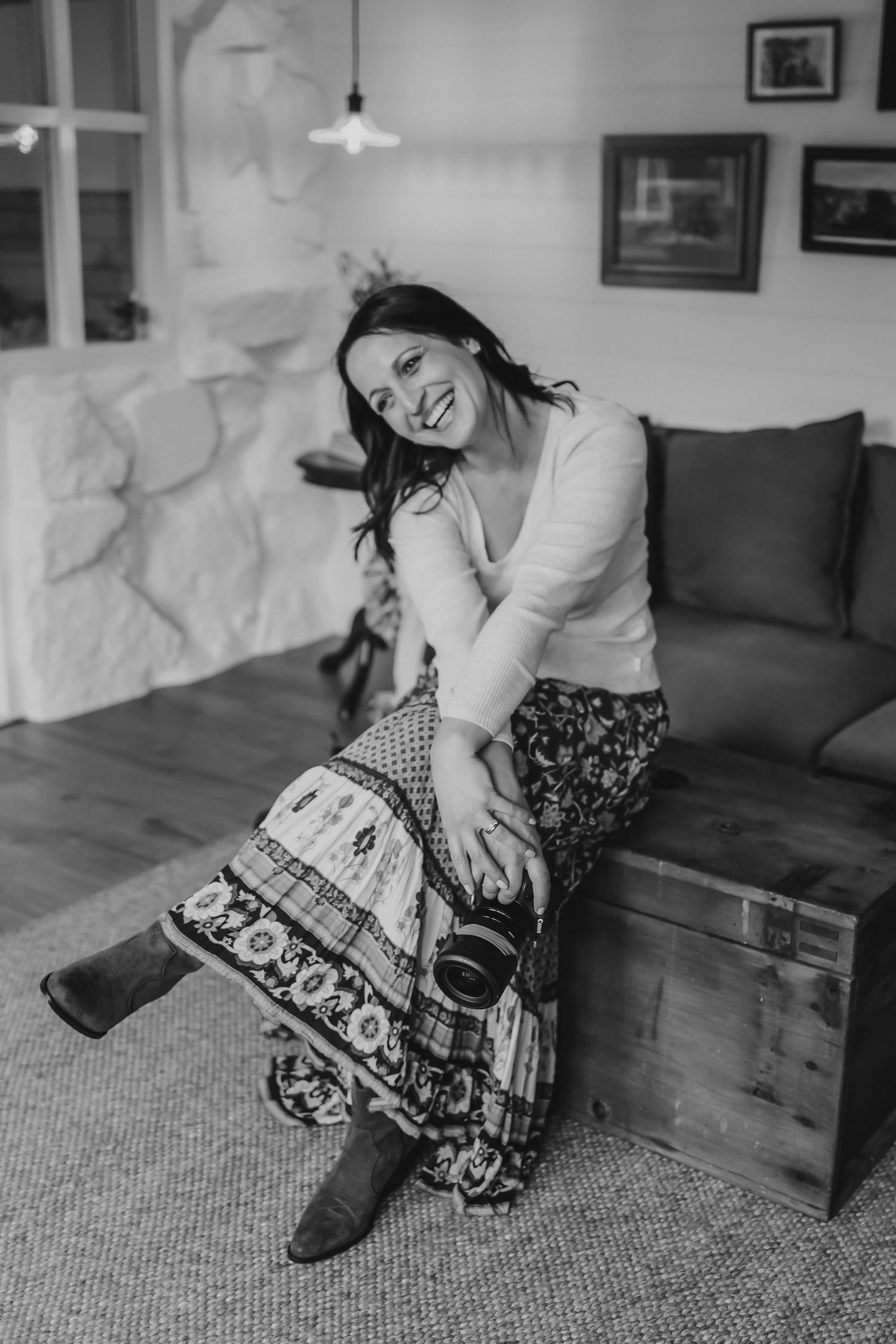 Black and white photo showing someone wearing a bohemian skirt sitting casually on a wooden chest in a cozy living room.