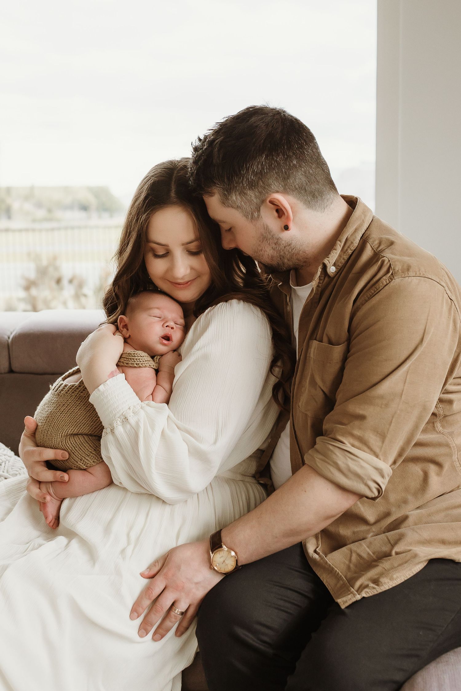 A series of tender family moments showing parents snuggling with a newborn baby on a couch in soft, neutral tones.