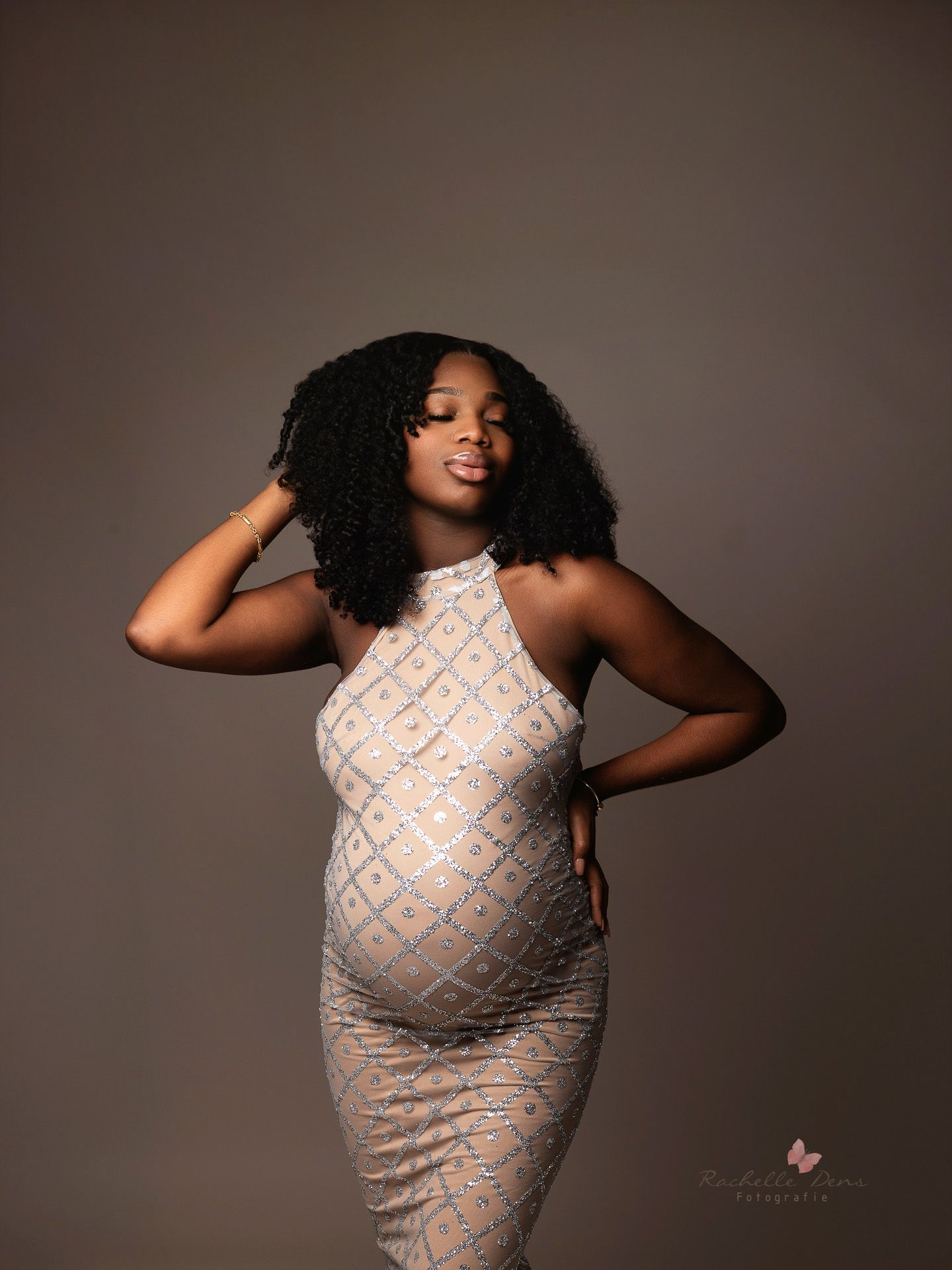 A maternity portrait featuring a fitted cream and silver patterned halter dress against a neutral backdrop.