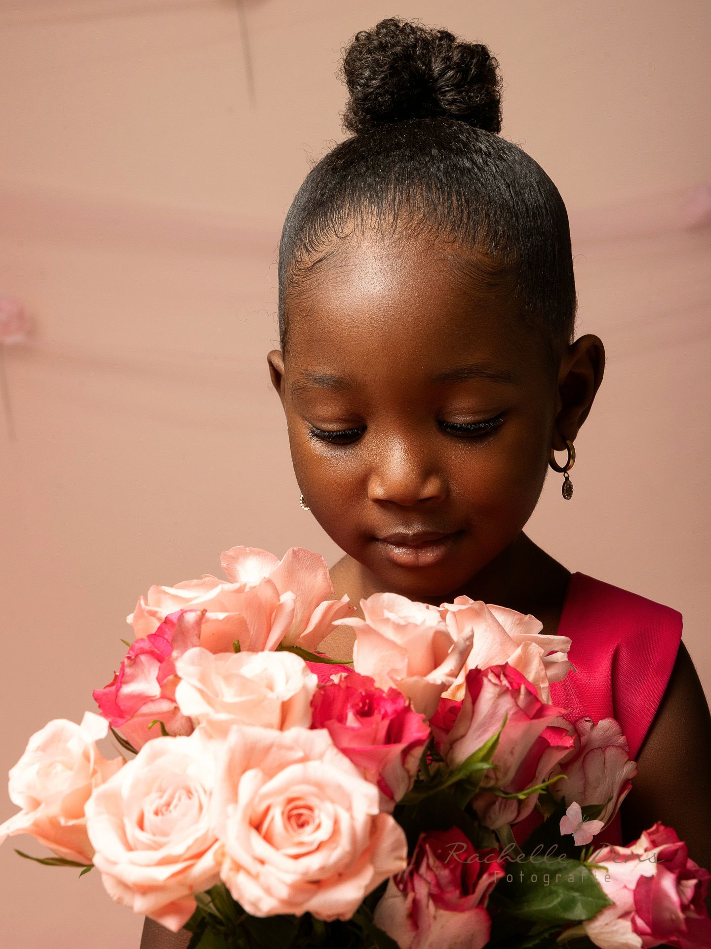 A person smiles while holding a bouquet of pink roses against a soft pink background.