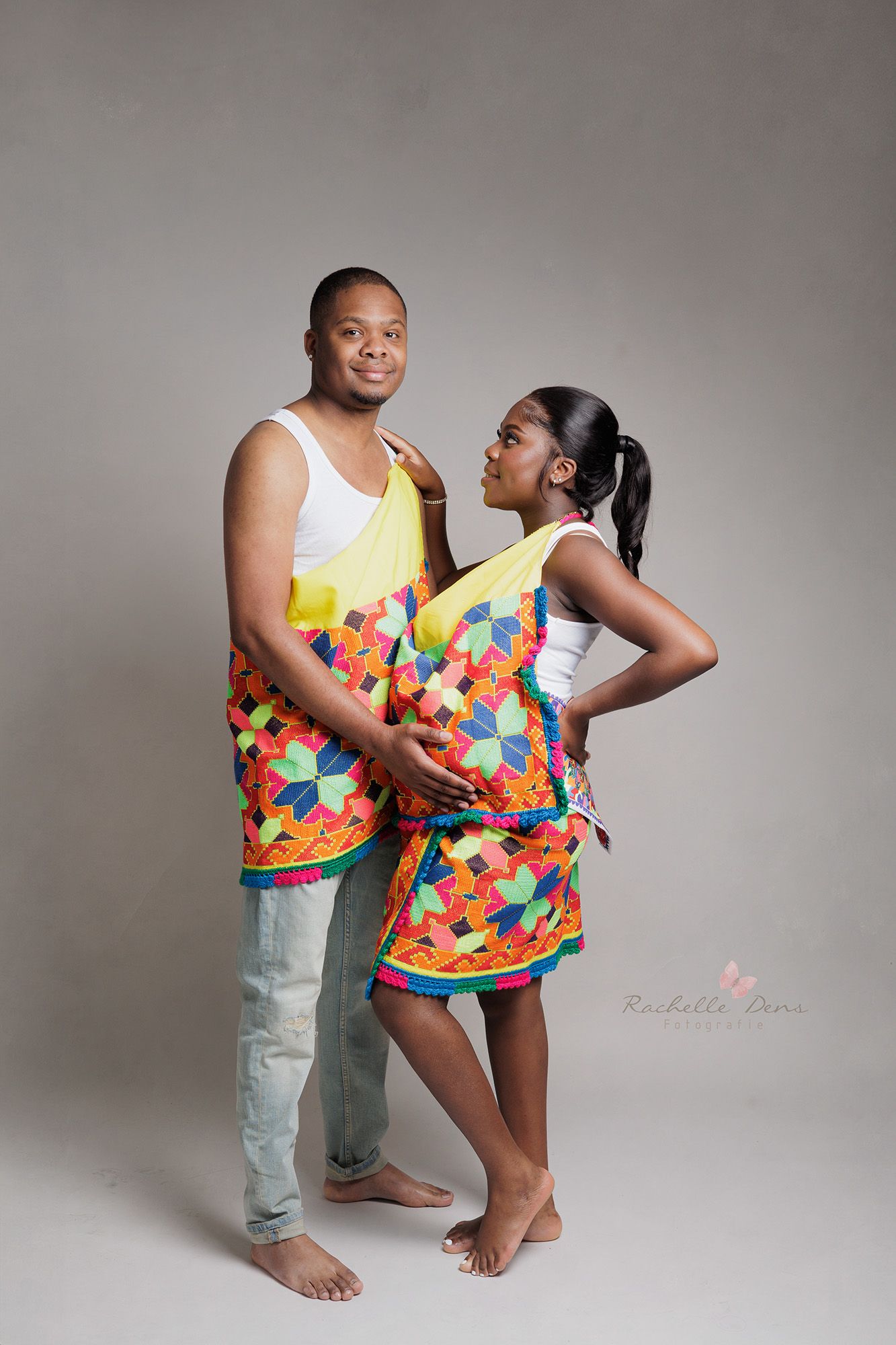 Two people in matching floral tank tops pose playfully together in a studio setting.