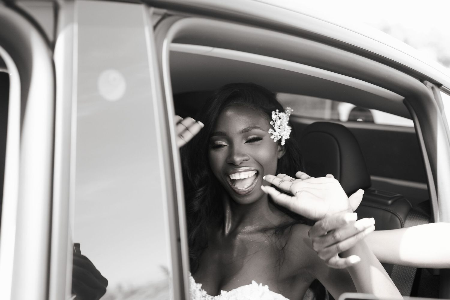 A group of wedding party members smile and laugh while seated in a classic car during a celebration.