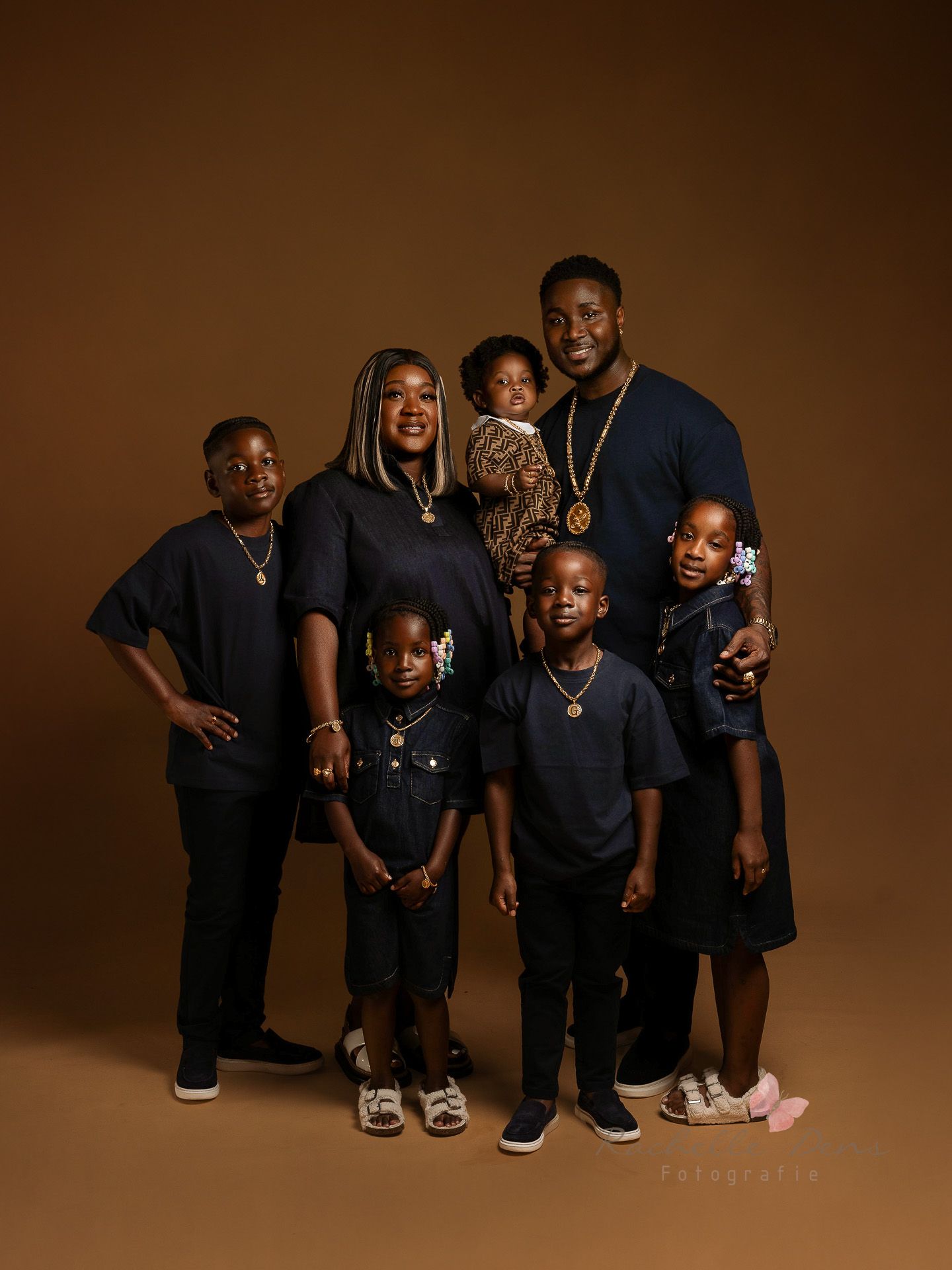 A family portrait series against a warm brown backdrop showing playful poses and coordinated black outfits.