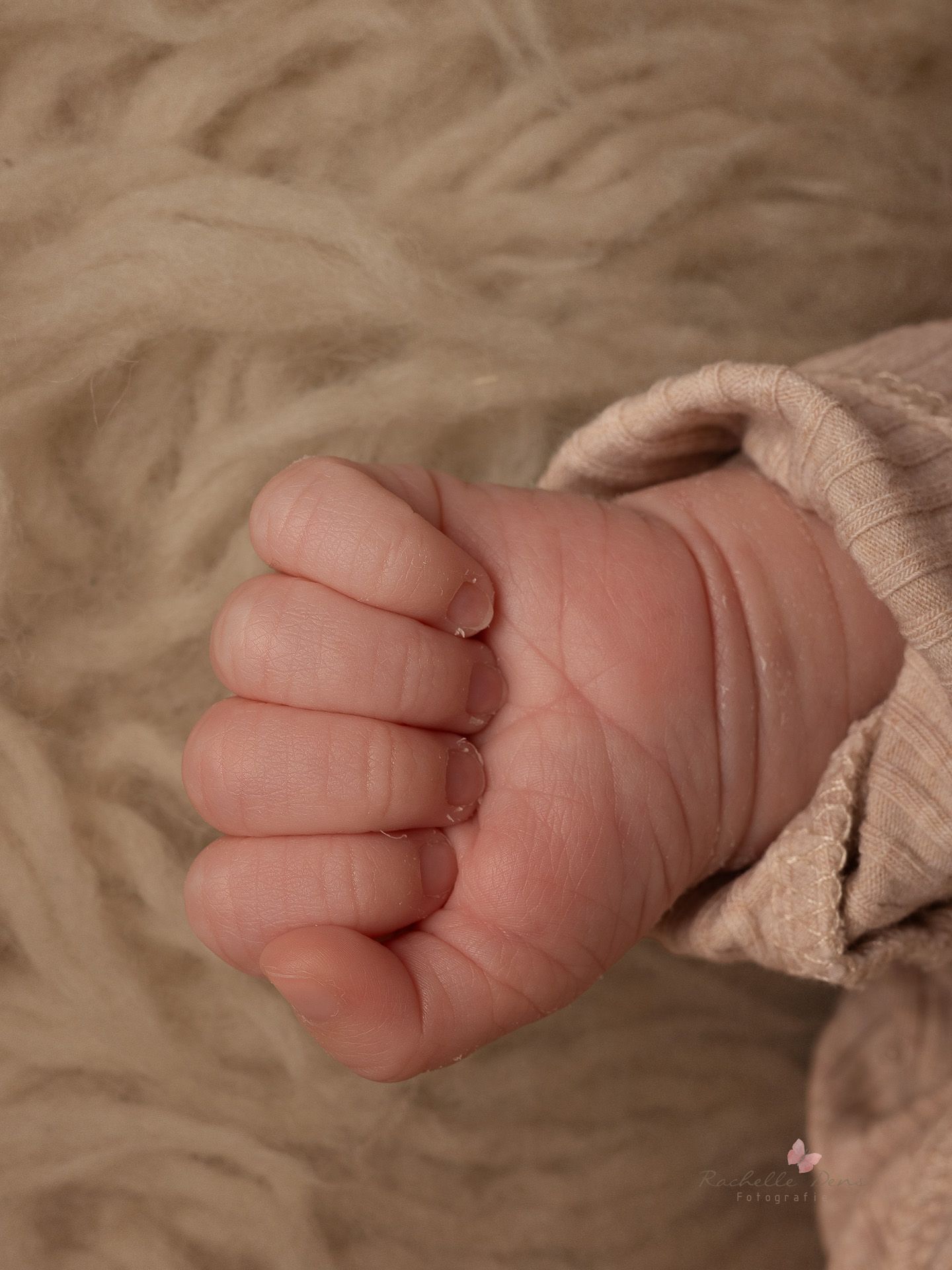 Close-up view of a tiny baby's foot wrapped in soft beige fabric against a textured background.