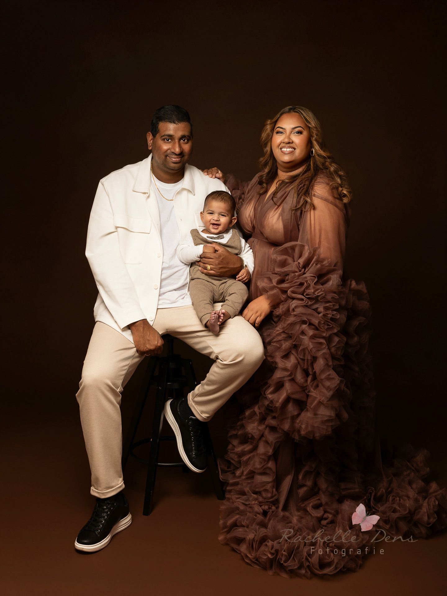 A family portrait series against a dark background featuring parents and baby in coordinating brown and white outfits.