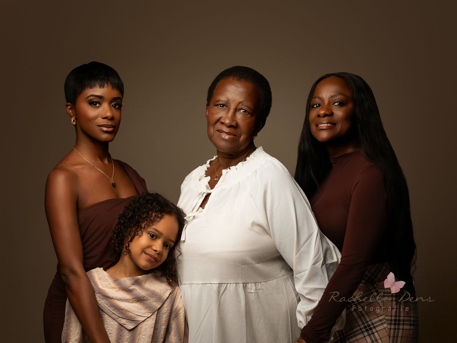 A multi-generational family portrait against a dark background featuring four people in brown and white tones.