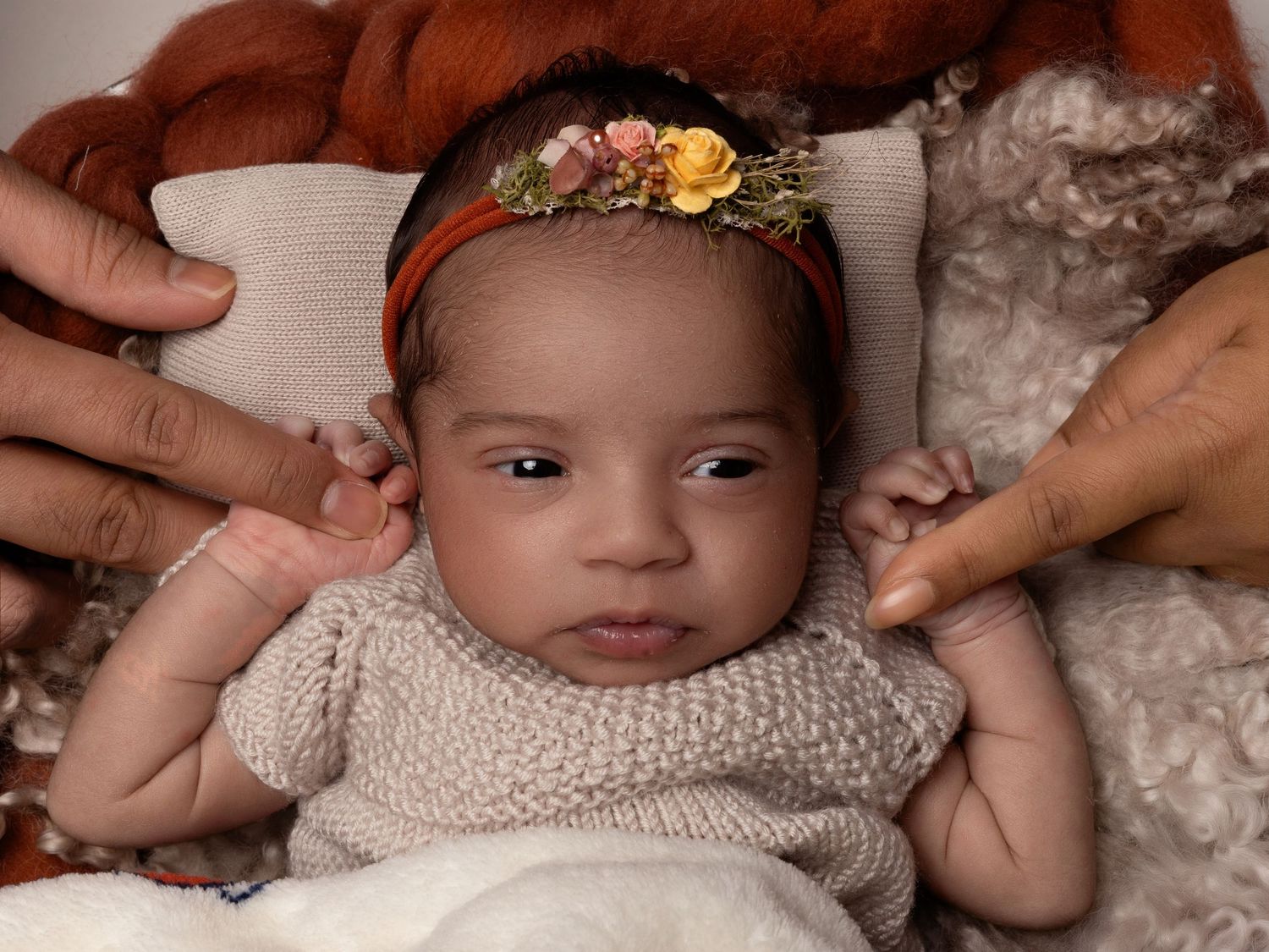 Baby wearing a delicate floral headband and cream knit sweater rests on soft blankets.