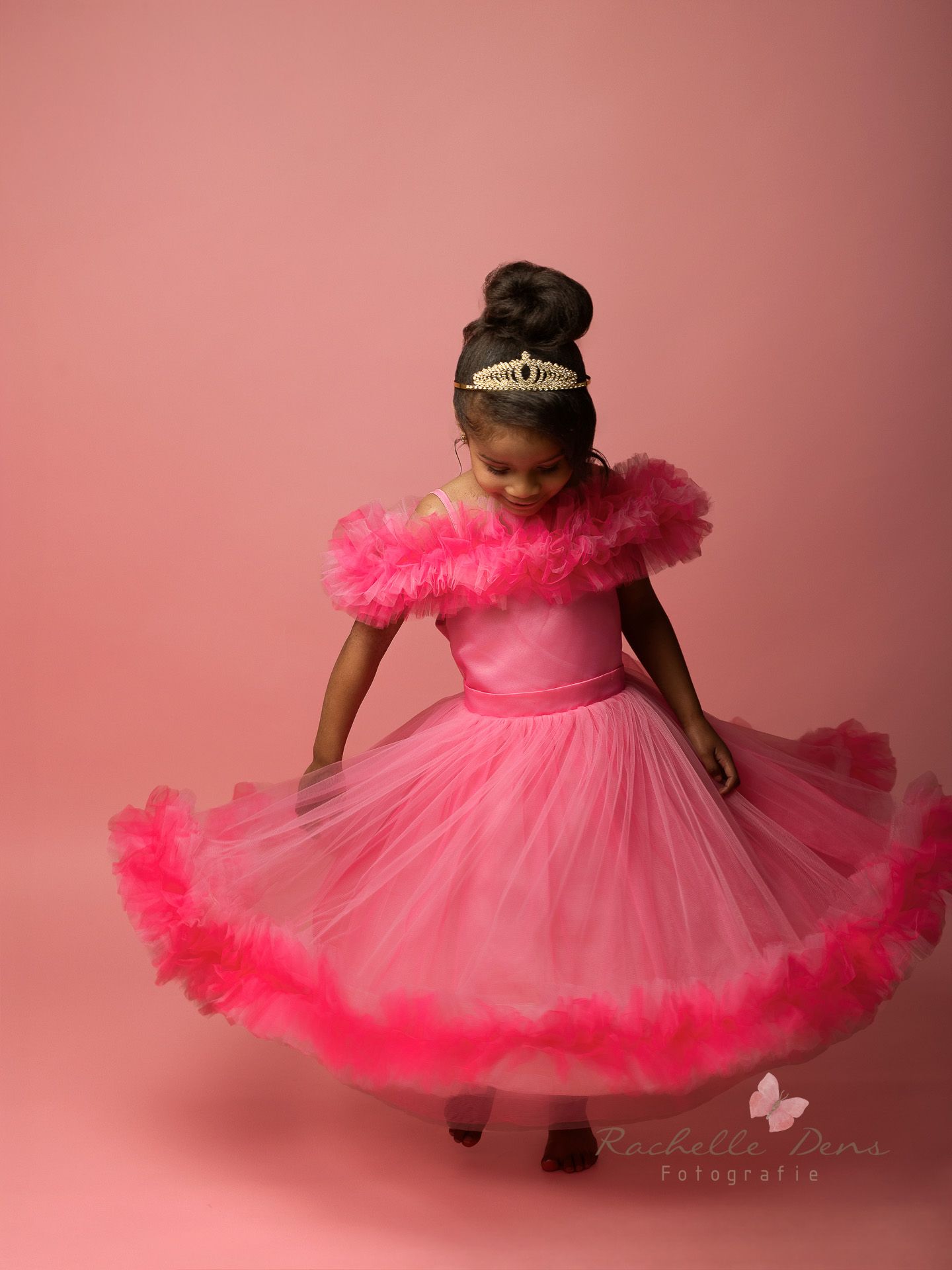 A young child in a fluffy pink tulle dress twirls gracefully against a pink studio backdrop.