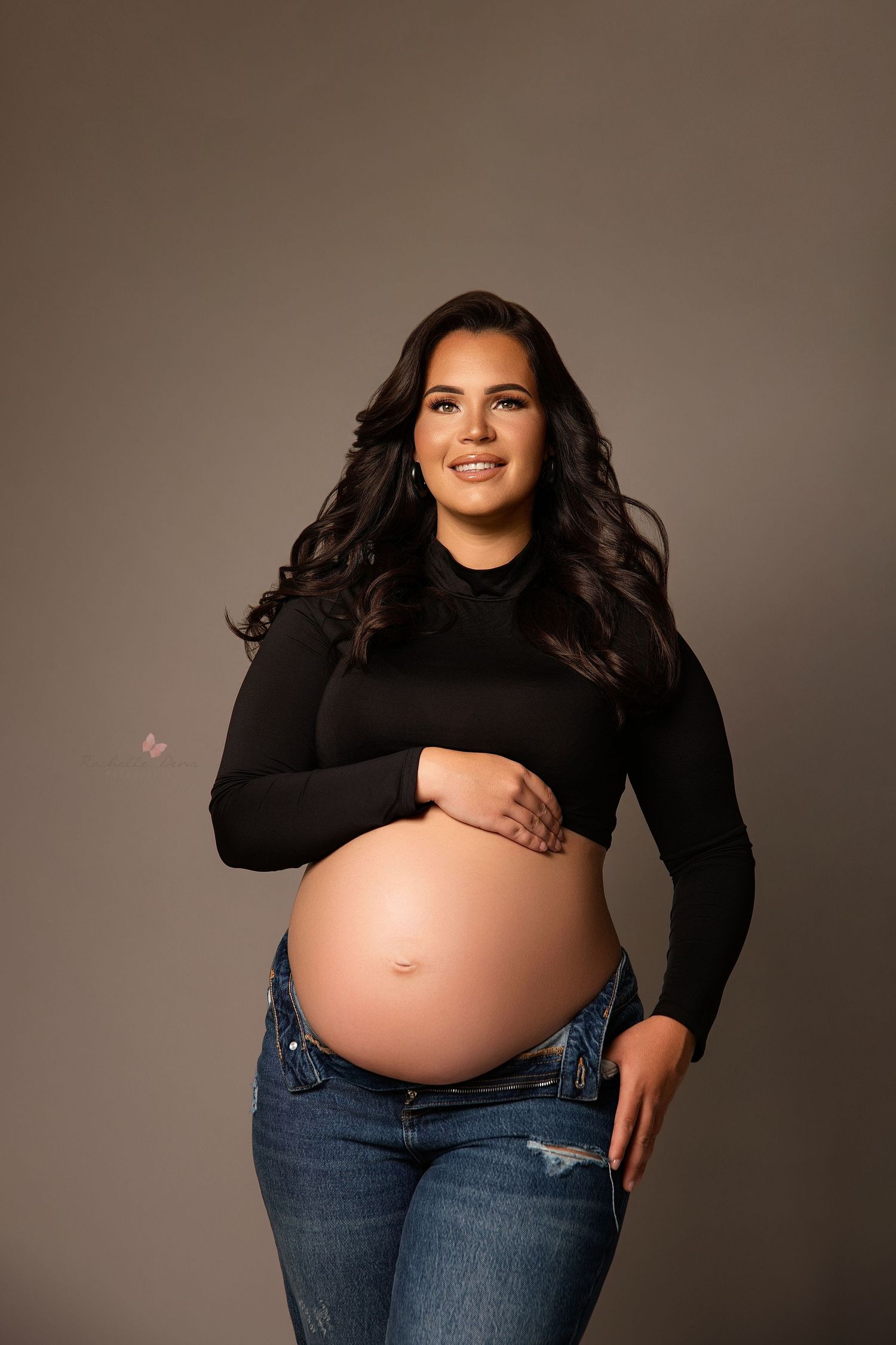 Maternity photo series showing pregnancy progression in black top and jeans against neutral studio backdrop.