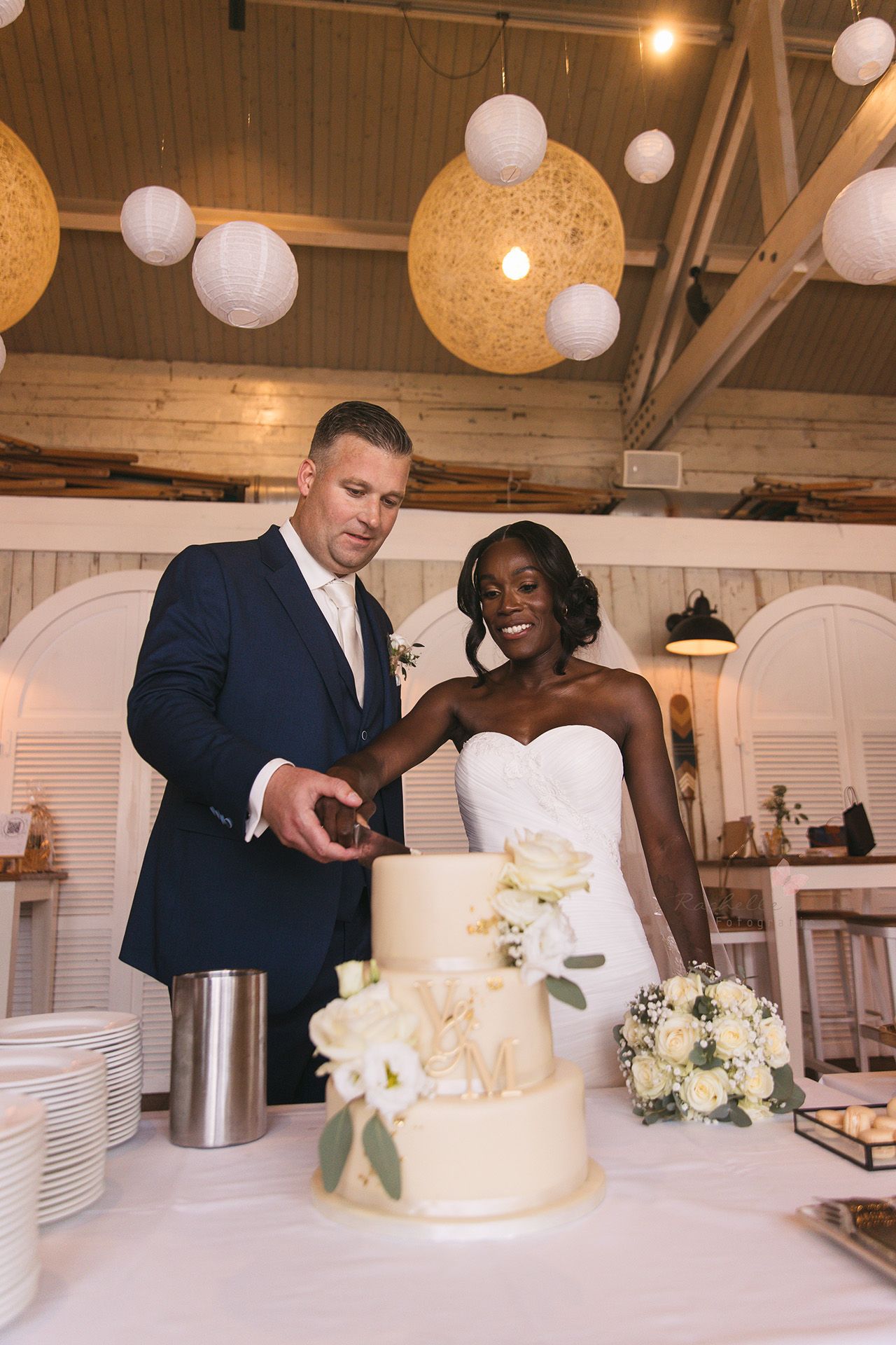 A couple cuts their elegant white wedding cake together at their reception decorated with paper lanterns.
