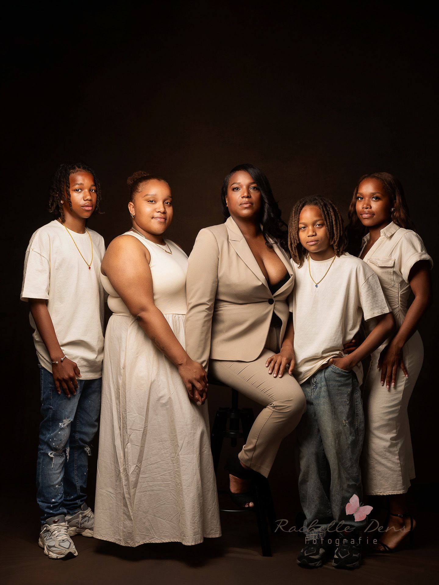 A group of people wearing coordinated white and beige outfits pose together against a dark backdrop in a studio setting.