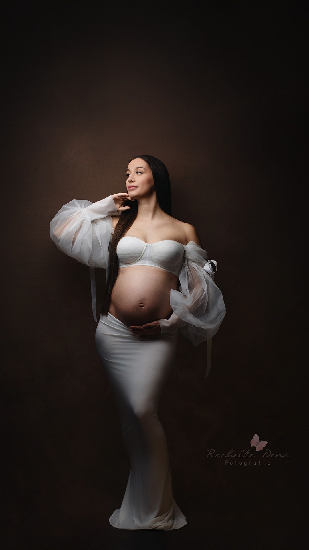 An elegant maternity portrait features a pregnant figure in flowing white fabric against a dark background.