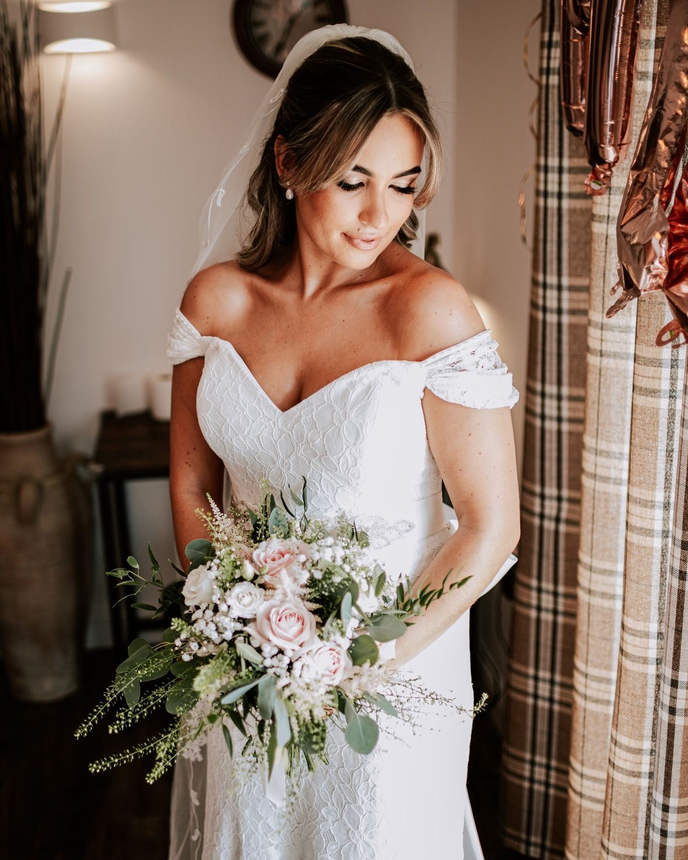 Bride in off-shoulder lace dress holding romantic bouquet with roses and greenery.