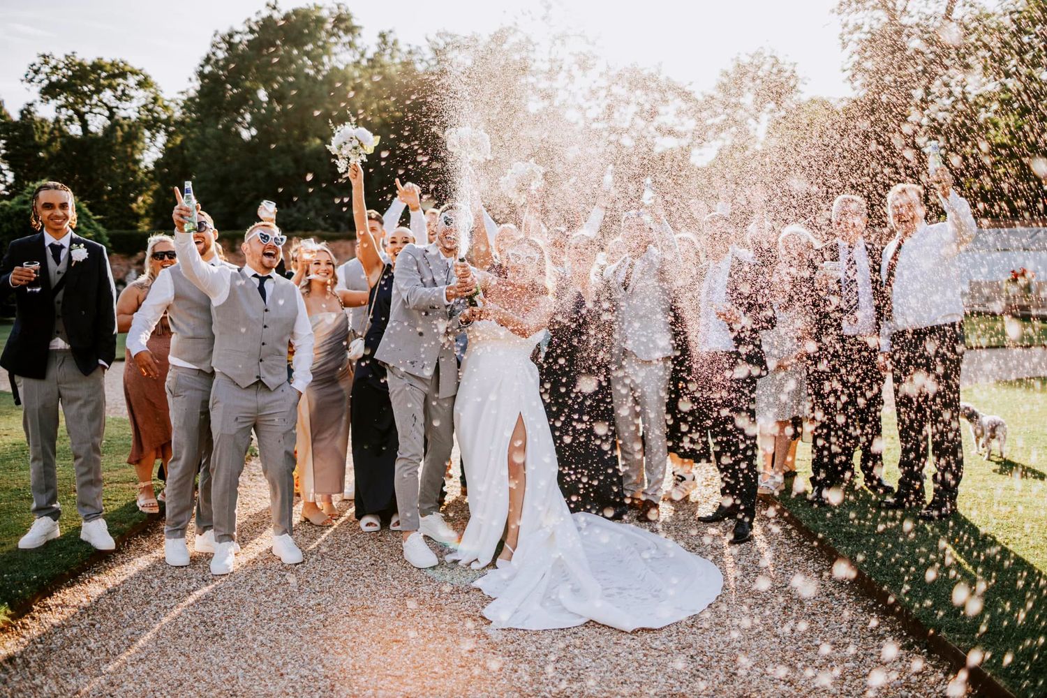Wedding party celebrates with confetti toss on outdoor path.