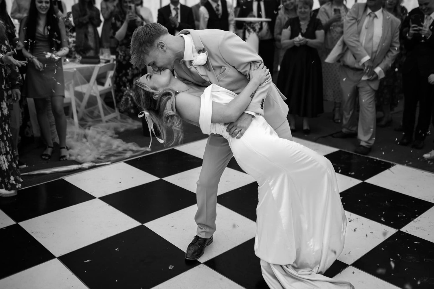 A dramatic black and white photo of a dance dip on a checkered floor during a wedding reception.