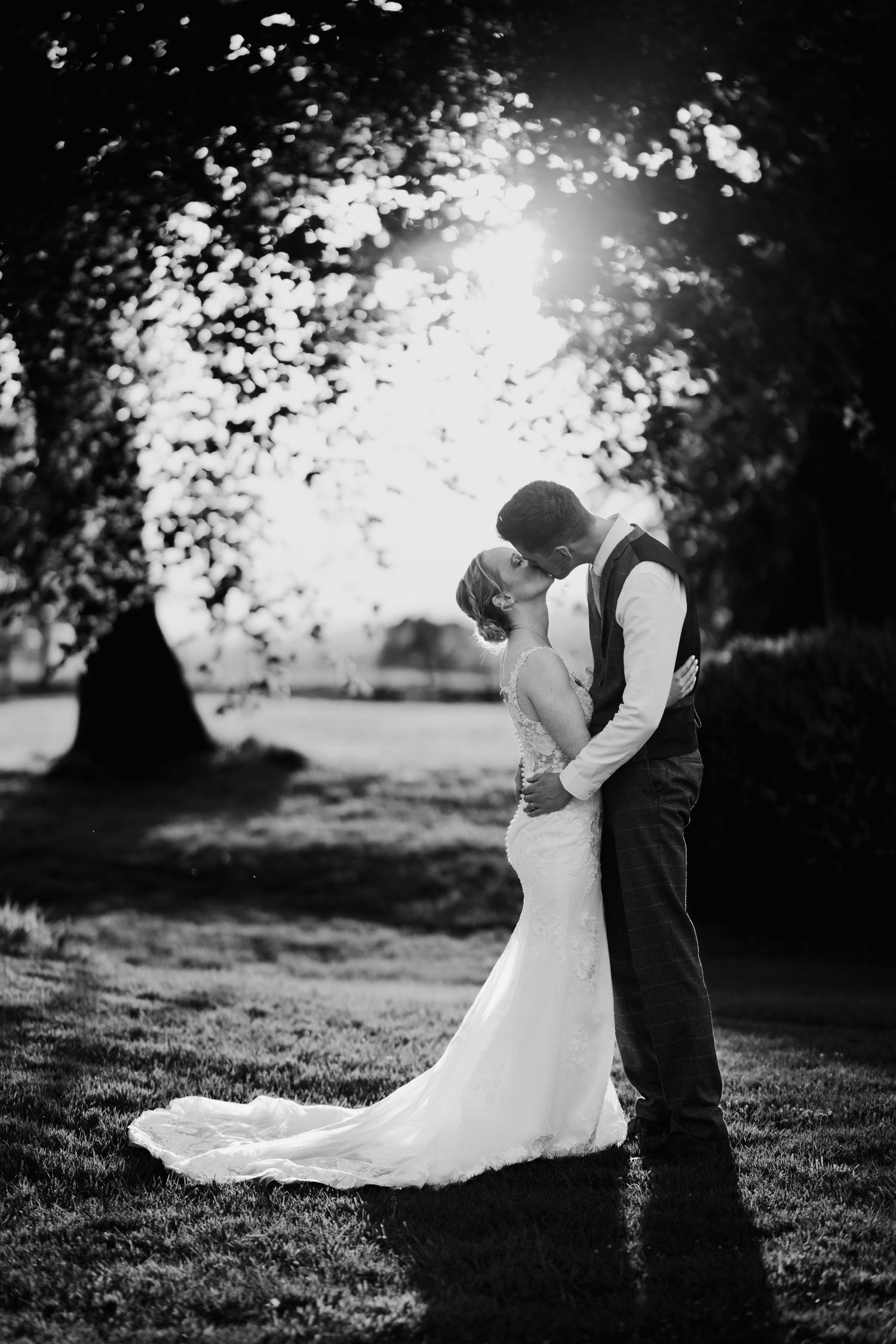 Black and white romantic portrait of couple embracing in dreamy backlit setting.