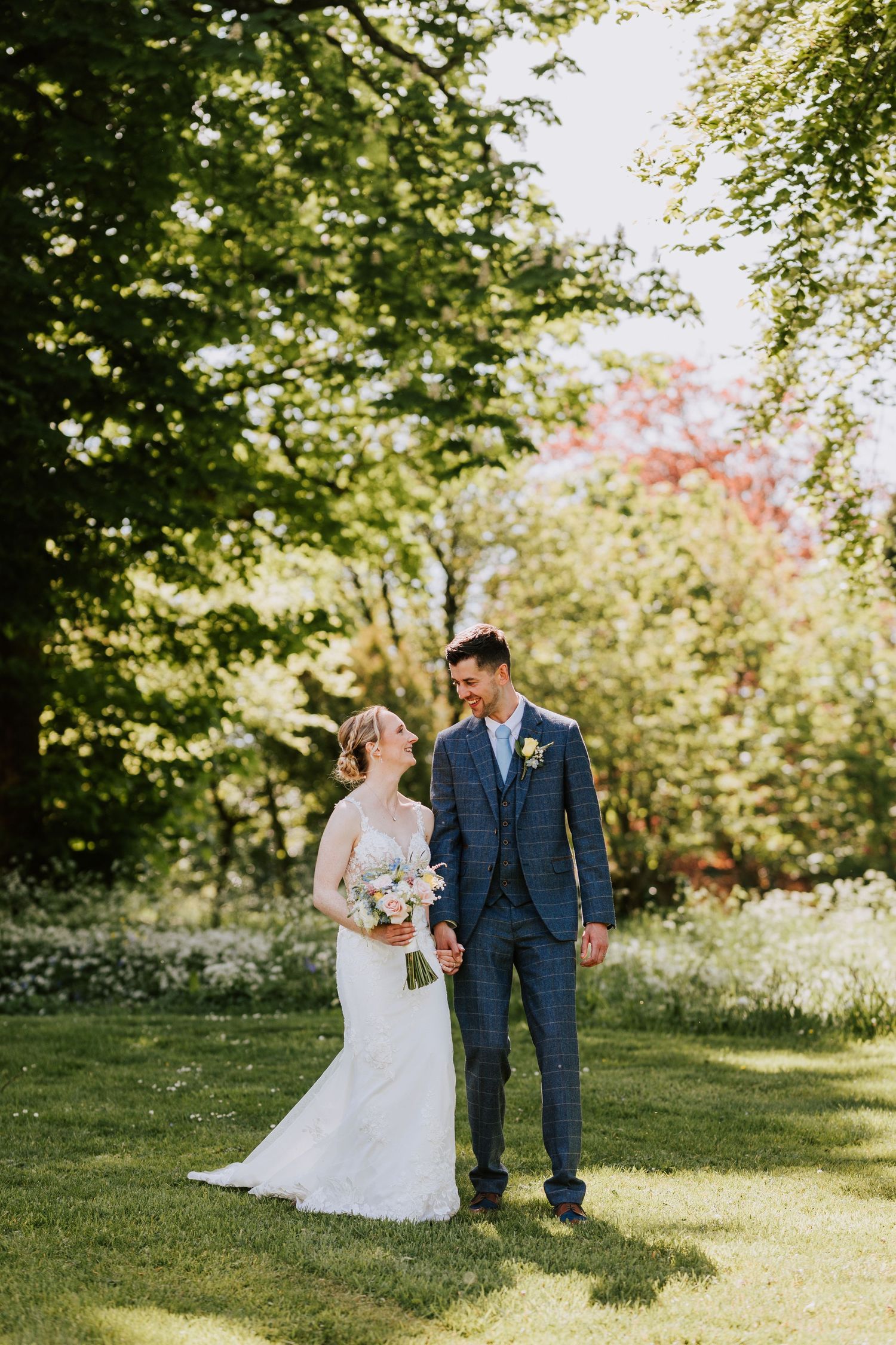 Wedding couple strolling through a verdant garden path on a sunny spring day.