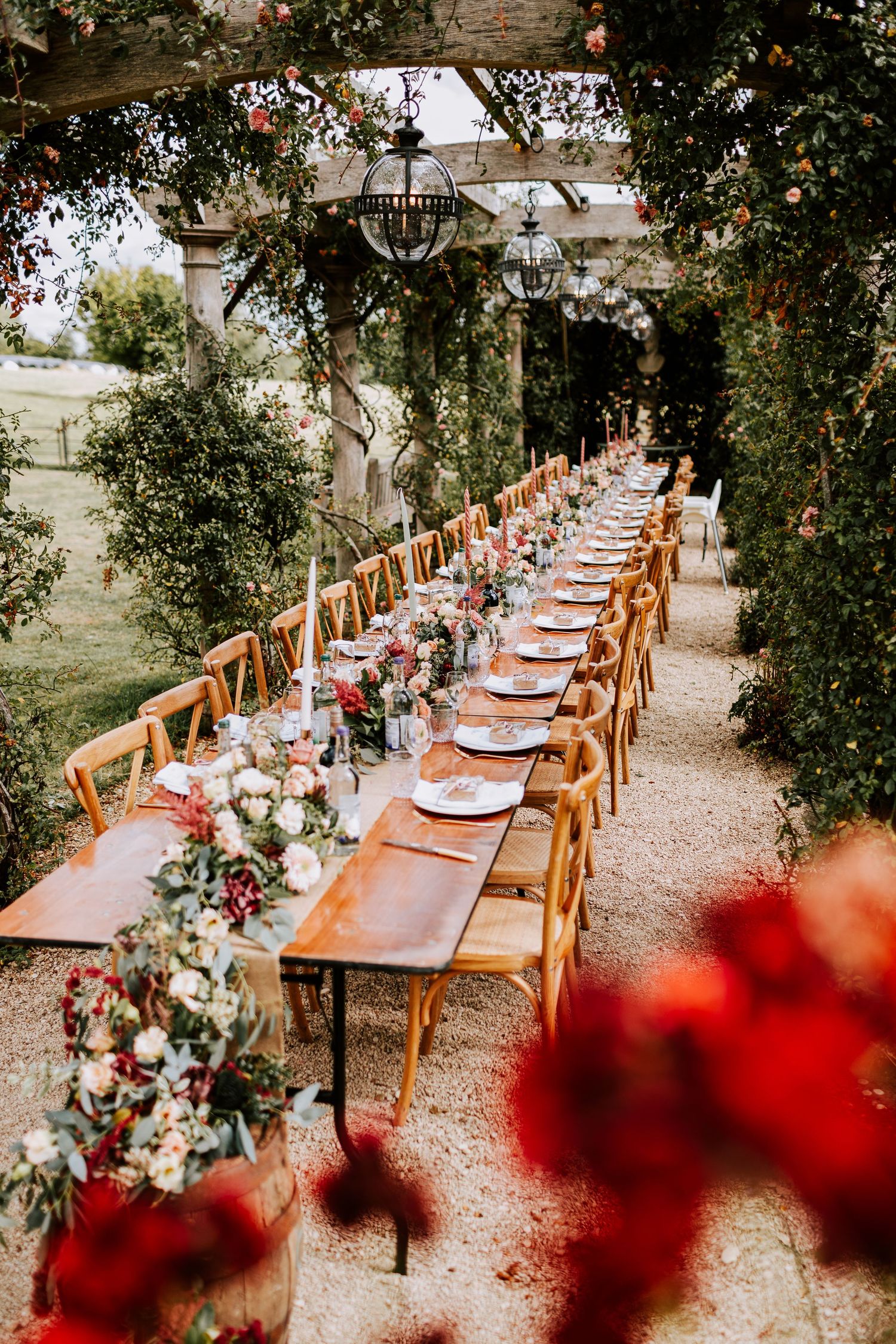 Elegant outdoor wedding reception table setting under pergola with floral decorations.