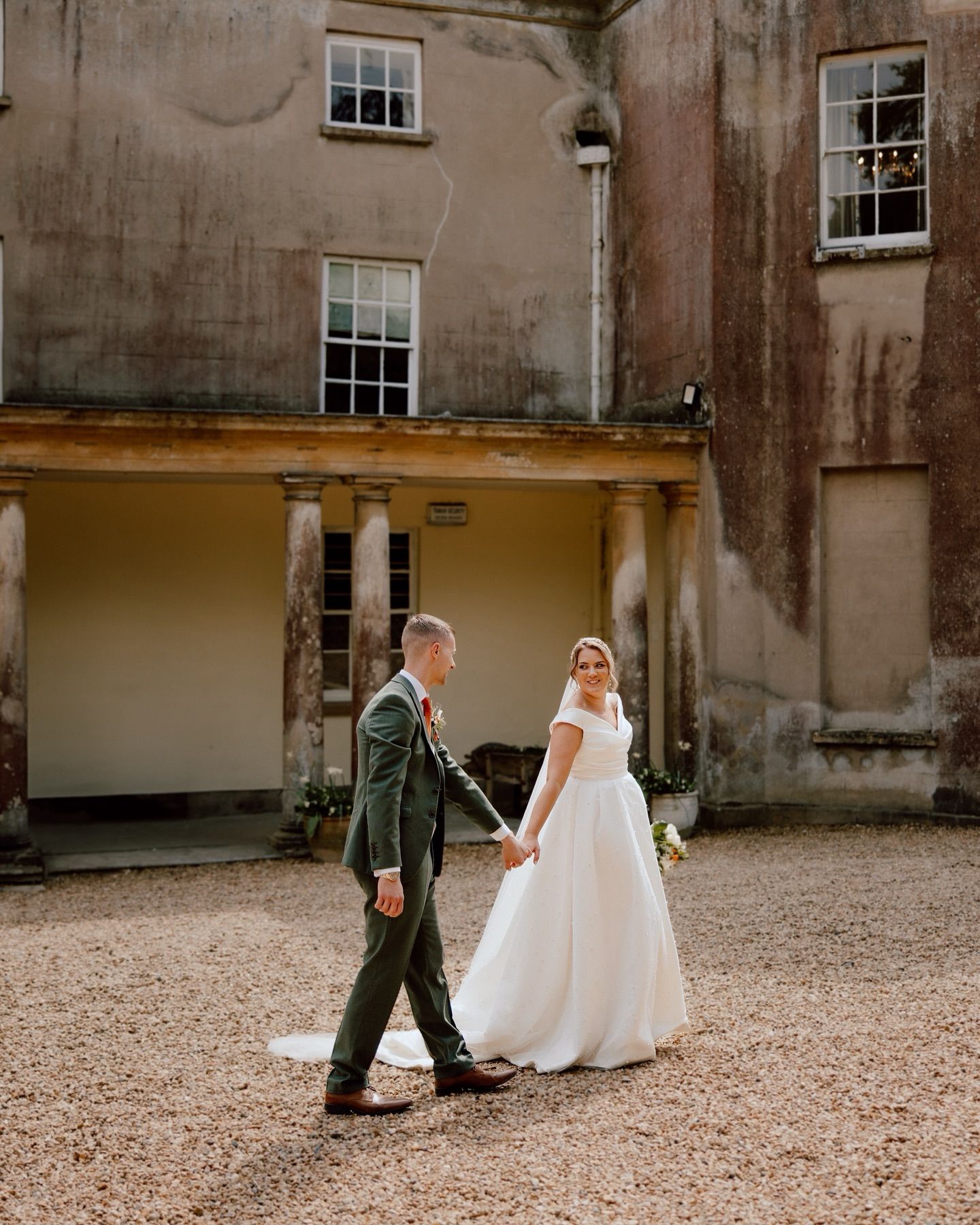 A couple walks outside a historic stone building with columns and weathered walls.