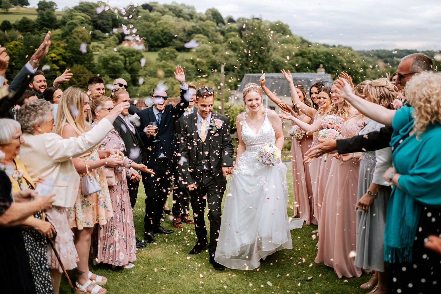 Wedding guests toss confetti as newlyweds celebrate outdoors.