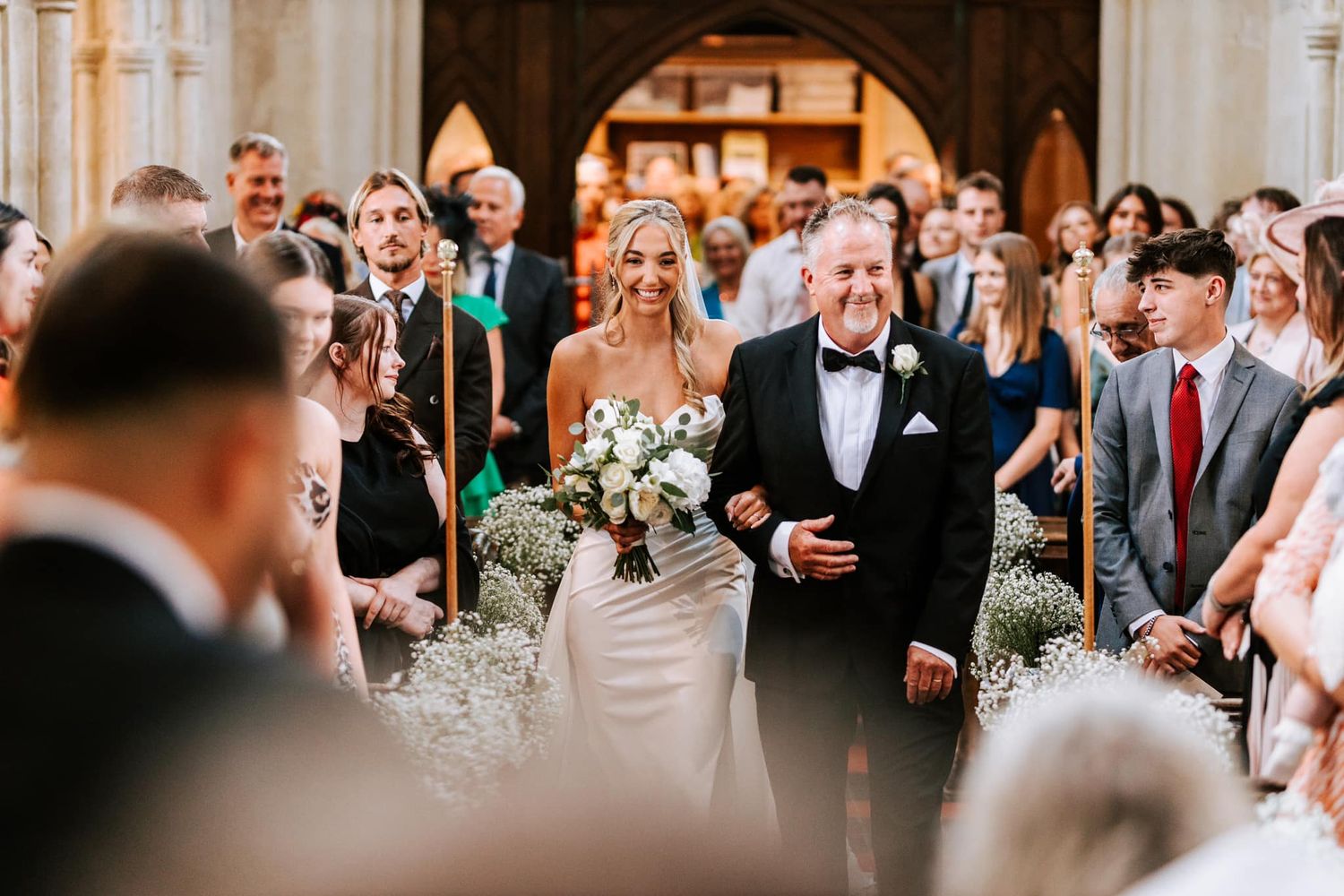 Joyful wedding ceremony procession in a church with guests lining the aisle.