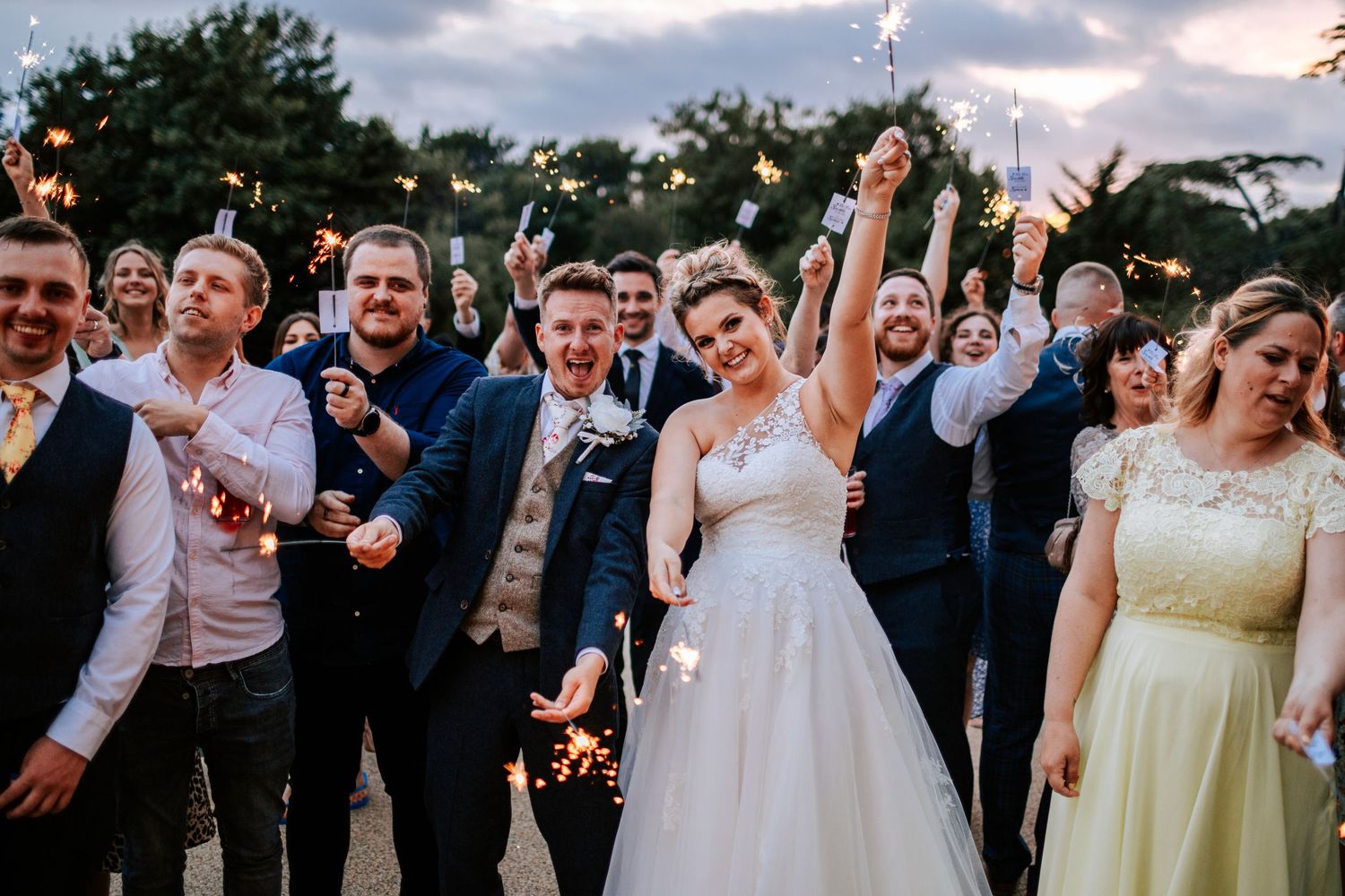 Wedding celebration with guests holding sparklers during an outdoor evening reception.