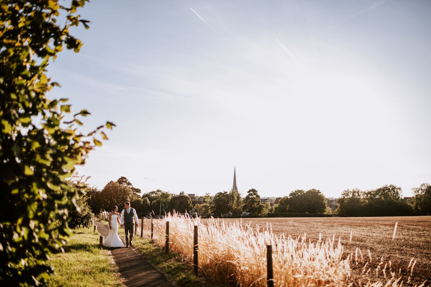 Scenic countryside path with church steeple visible in distance through autumn trees.