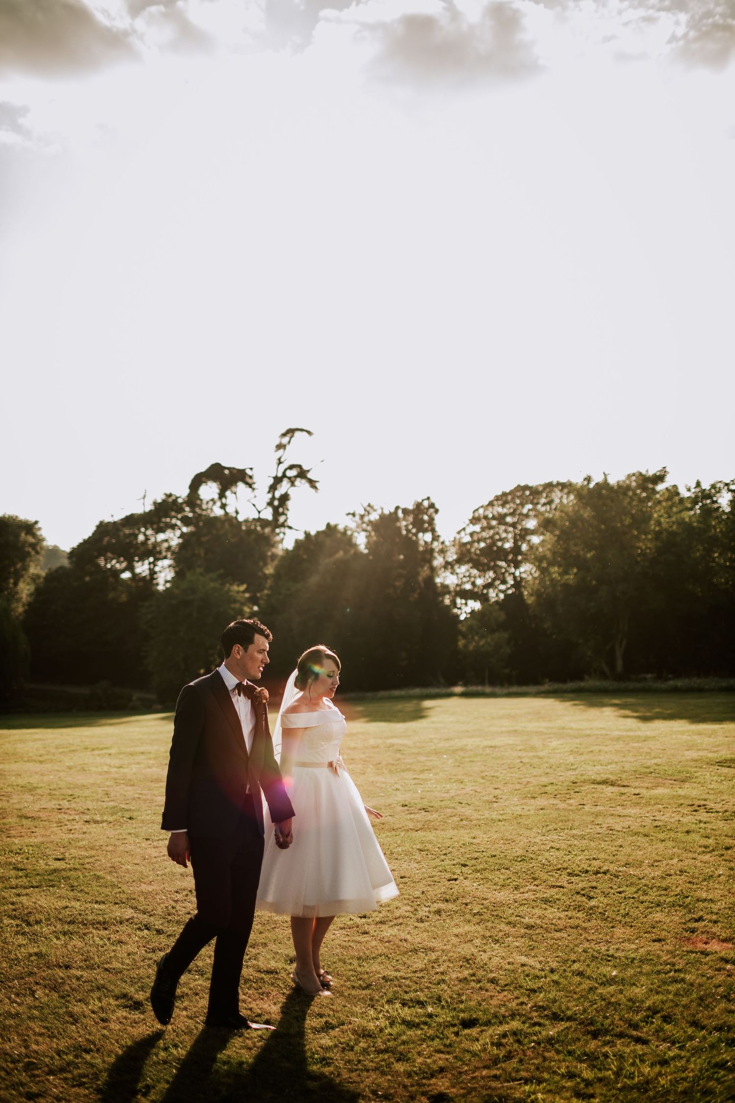 Silhouetted wedding couple walking through field at golden hour.