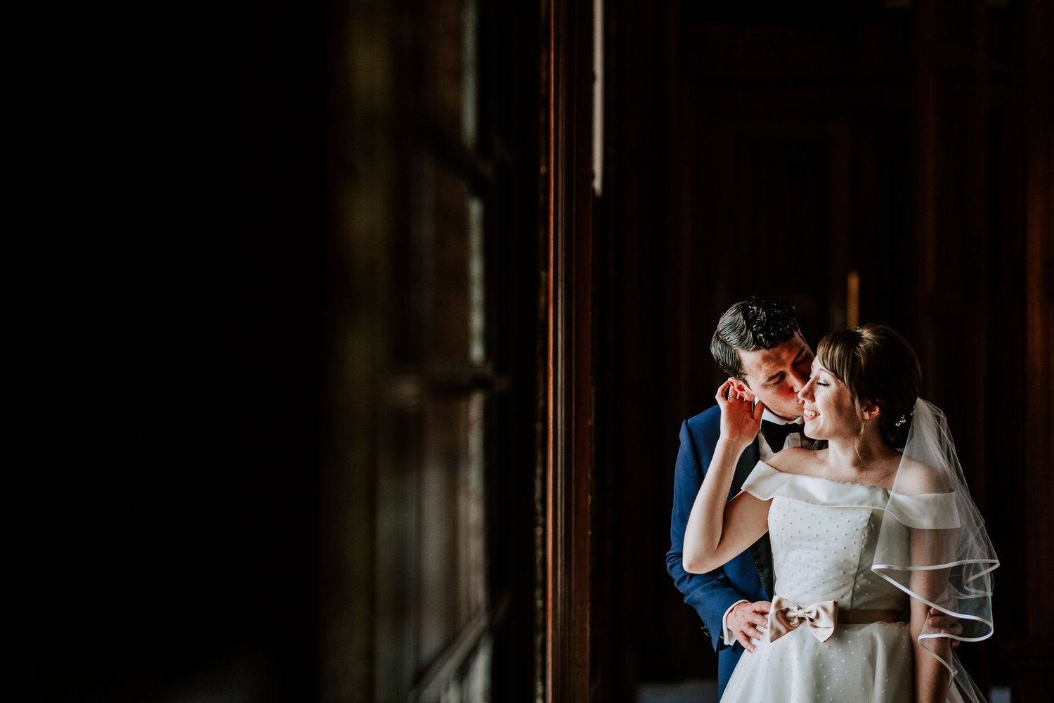 A romantic moment captured between two people by a window in dramatic lighting.