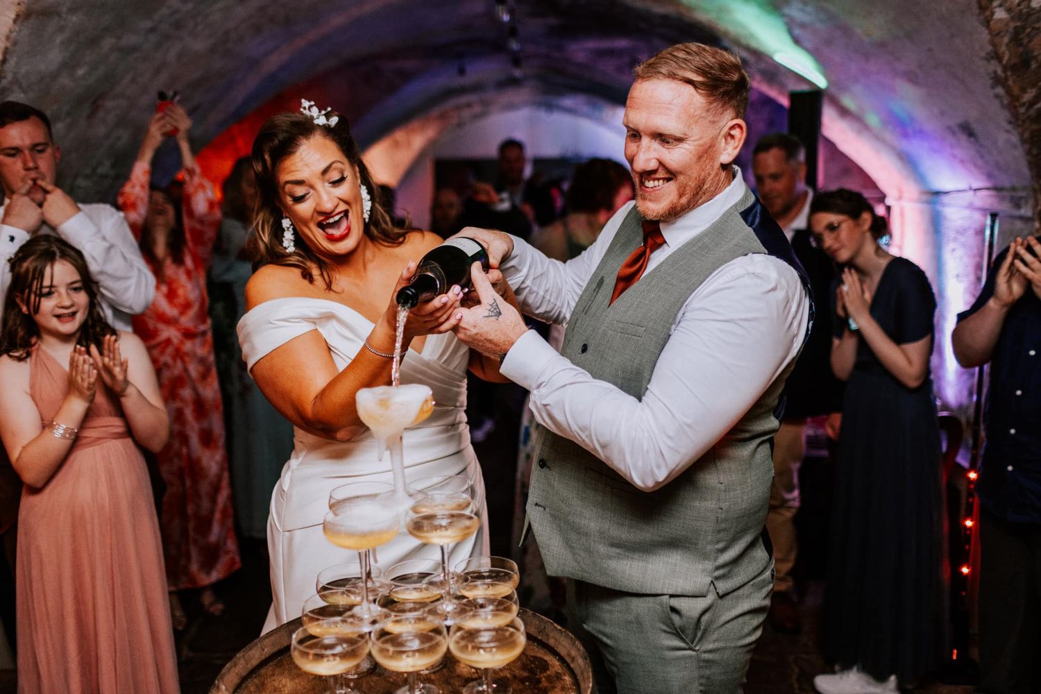 Wedding couple pours champagne tower at reception celebration.