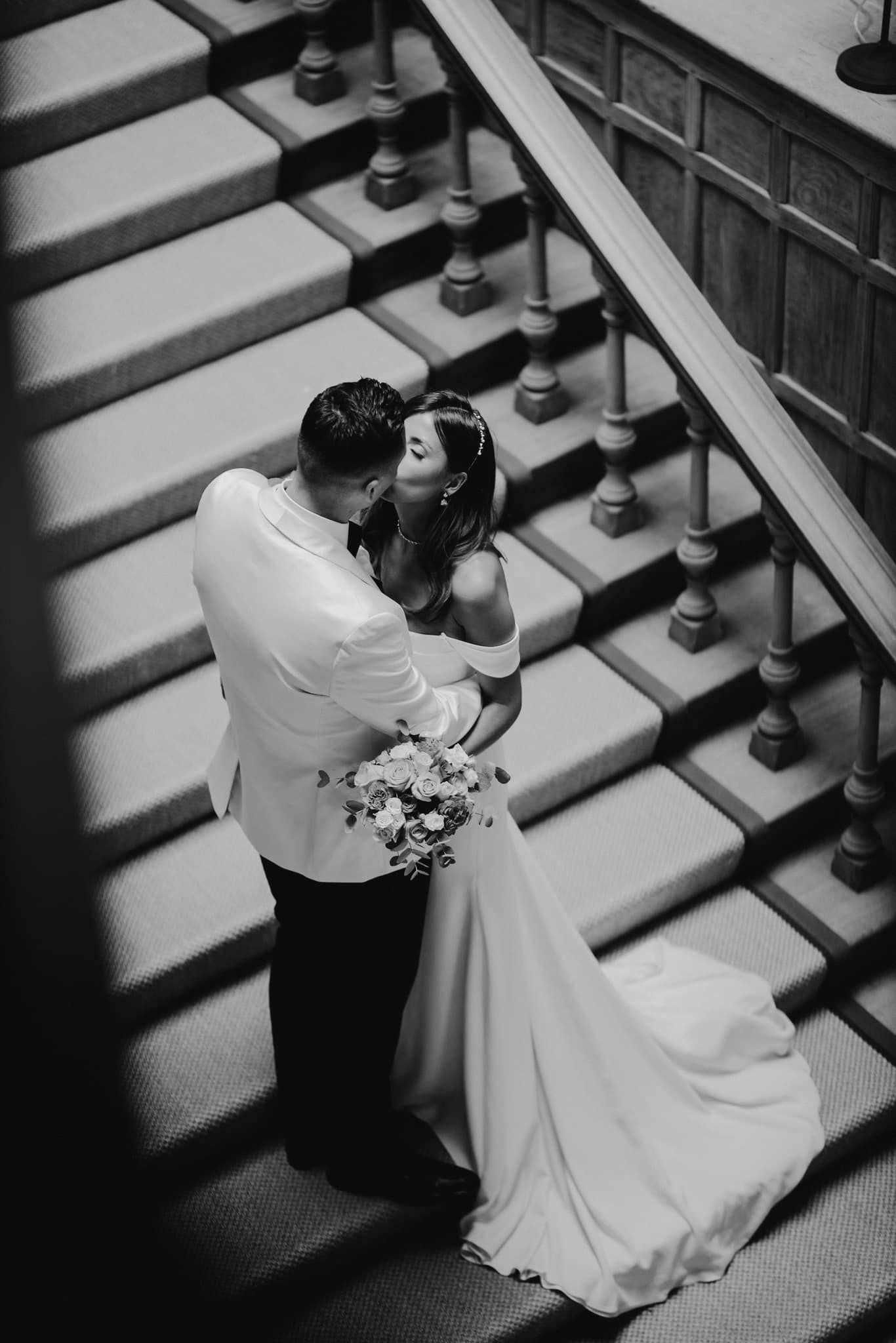 Black and white photo of romantic couple embracing on ornate staircase.