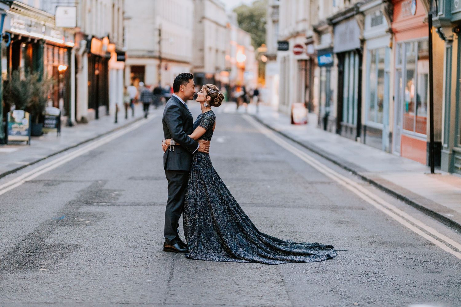 Wedding couple poses dramatically on cobblestone city street with flowing dress.