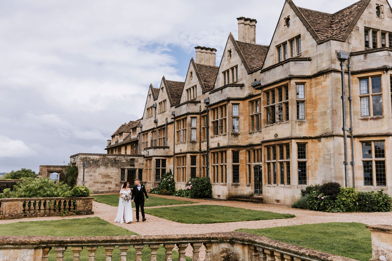 Wedding couple walking outside historic stone manor house with Gothic architecture.