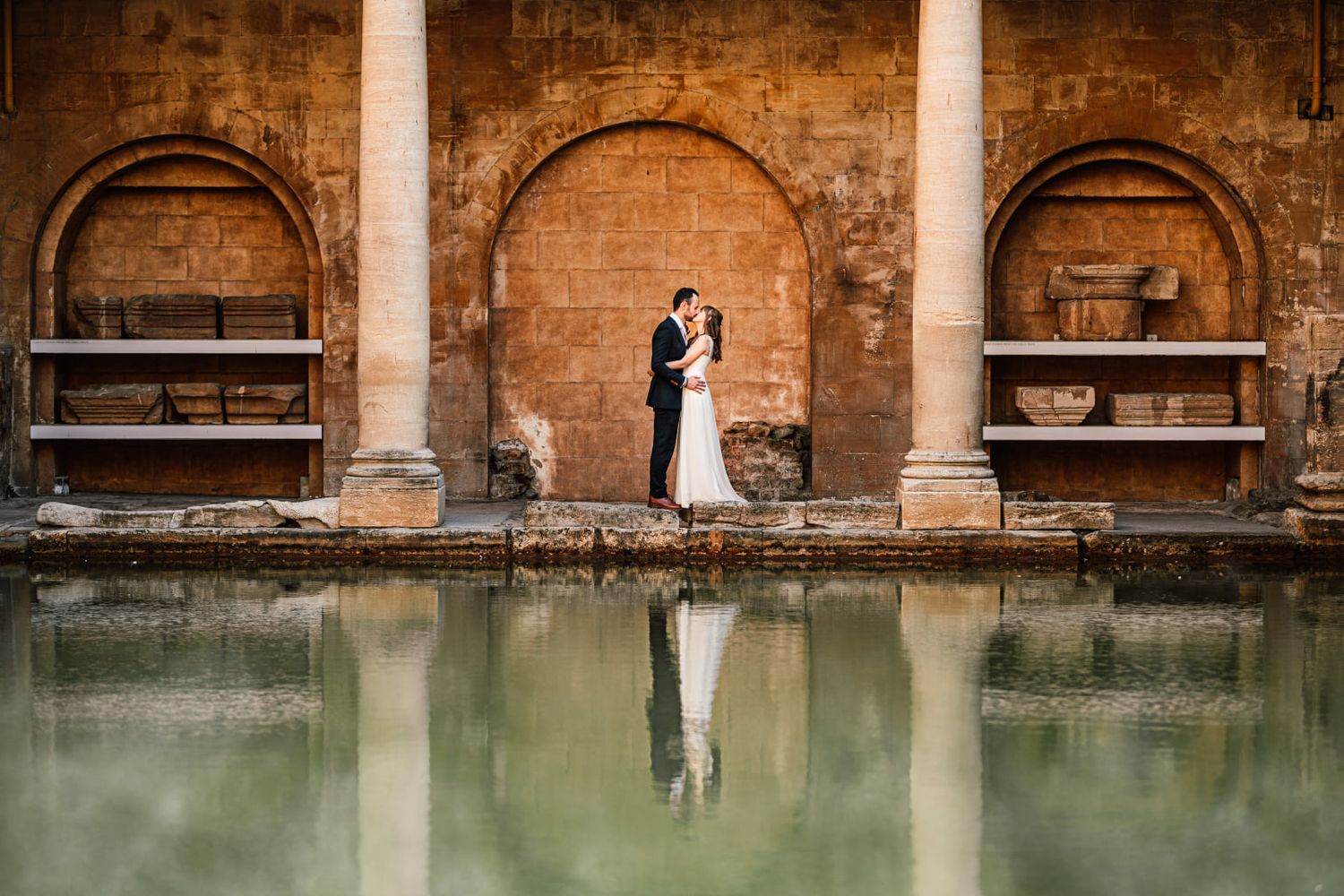 Historic brick architecture with columns and arches reflects in calm green water, creating a vintage atmosphere.
