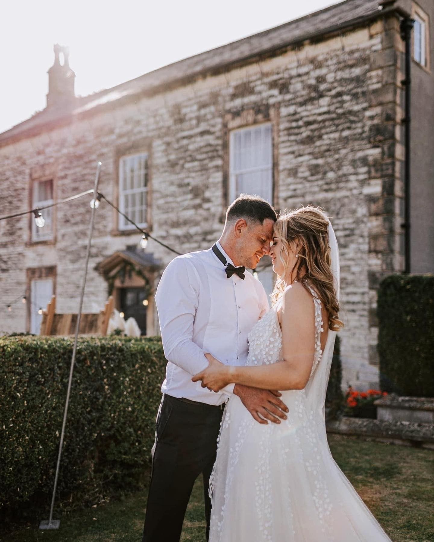 Romantic sunset portrait against stone building with couple in classic wedding attire.
