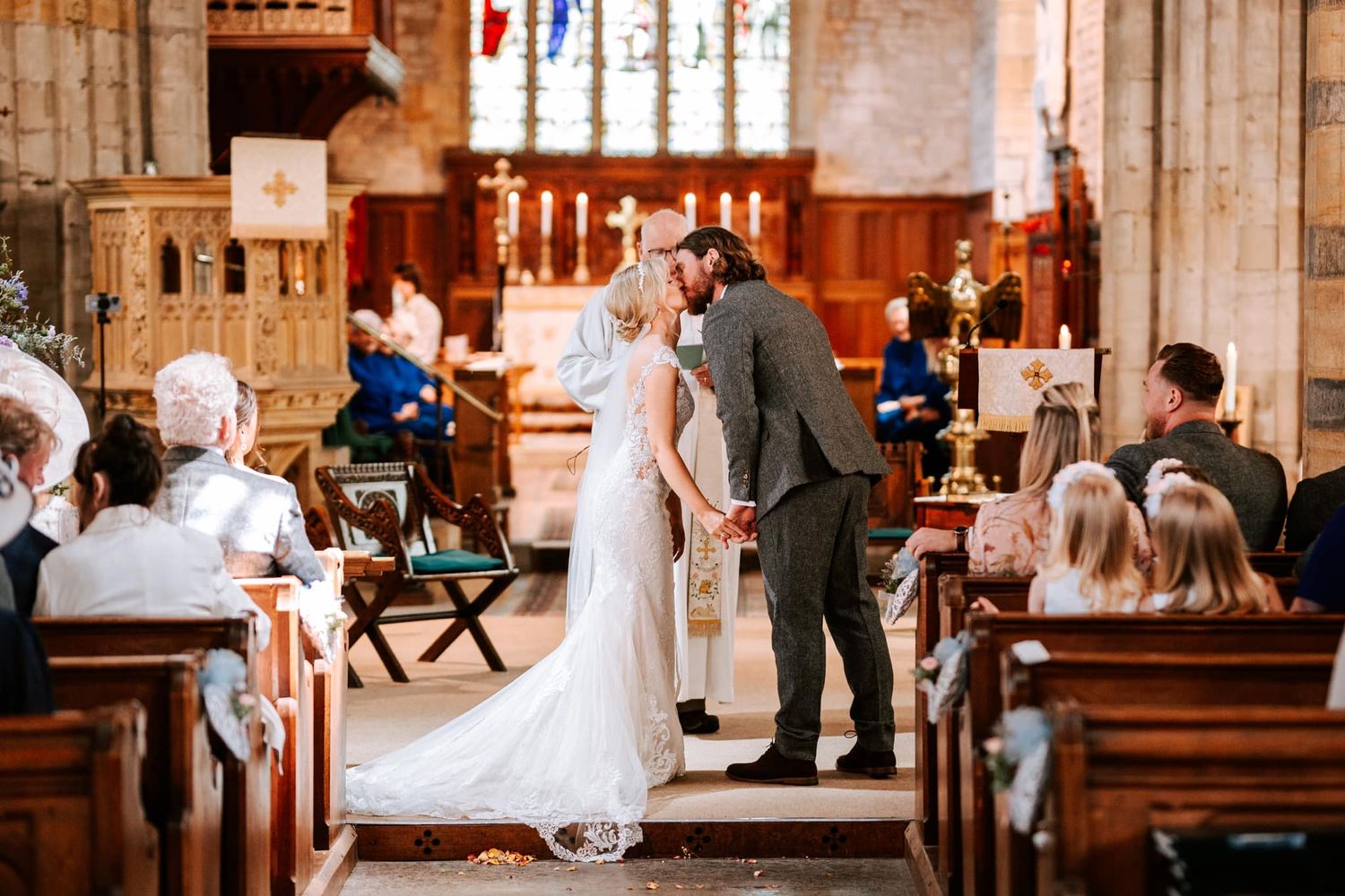 Wedding ceremony in traditional church with wooden pews and stained glass windows.