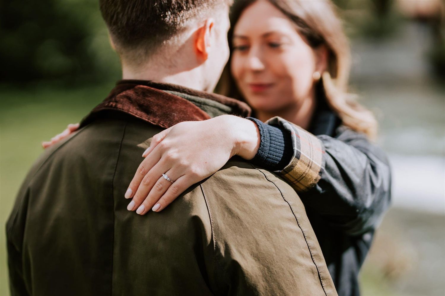 Close-up view of a couple embracing, showing a smartwatch and engagement ring.